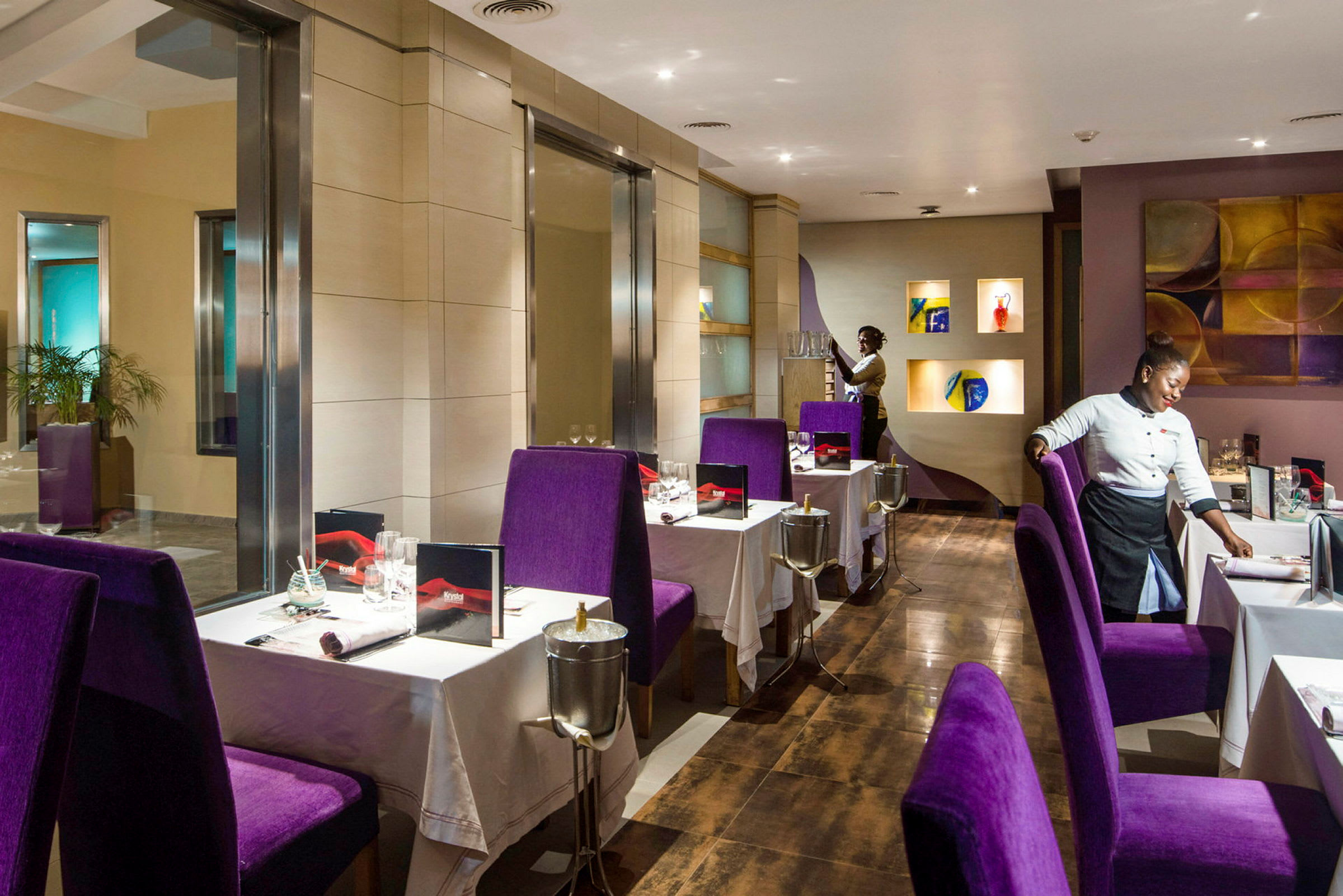 Bilde av en elegant innredet restaurant med lilla stoler og hvite duker, samt servitører som klargjør bordene. (AI-generert tekst)