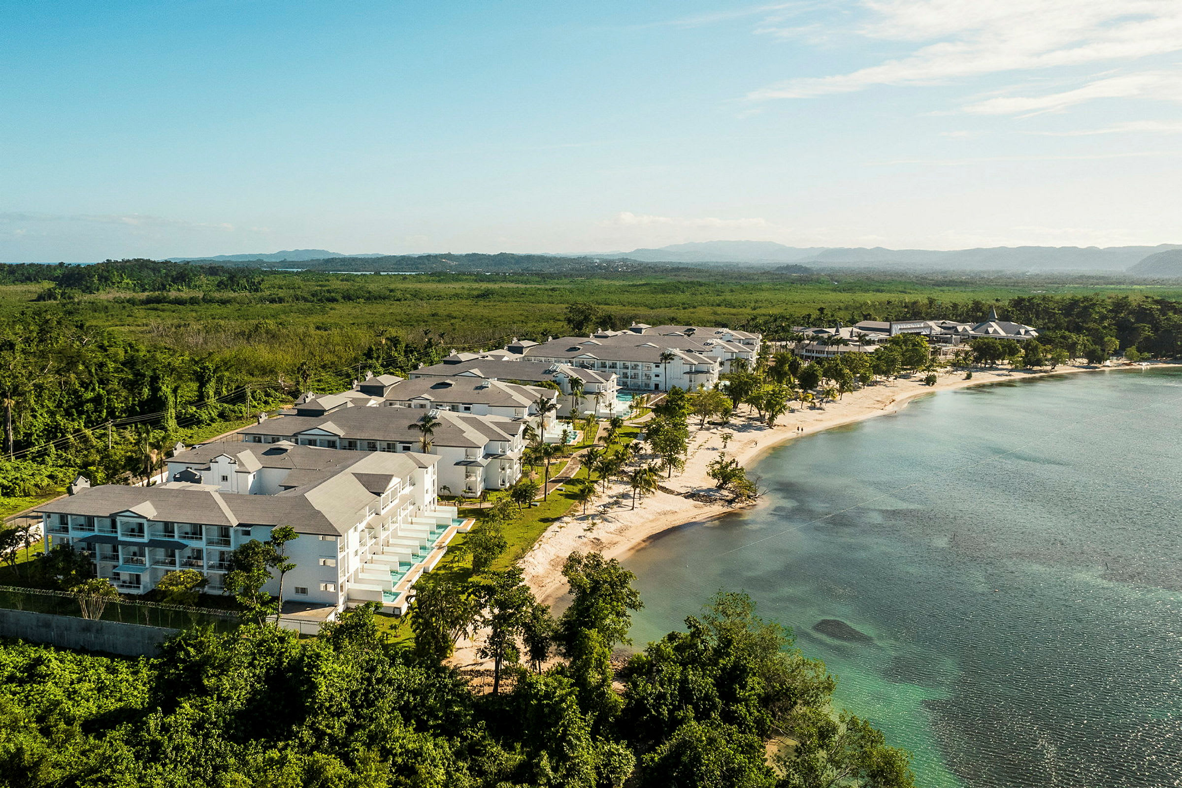 Et strandområde med resortbygninger omgitt av grøntområder og hav. (AI-generert tekst)