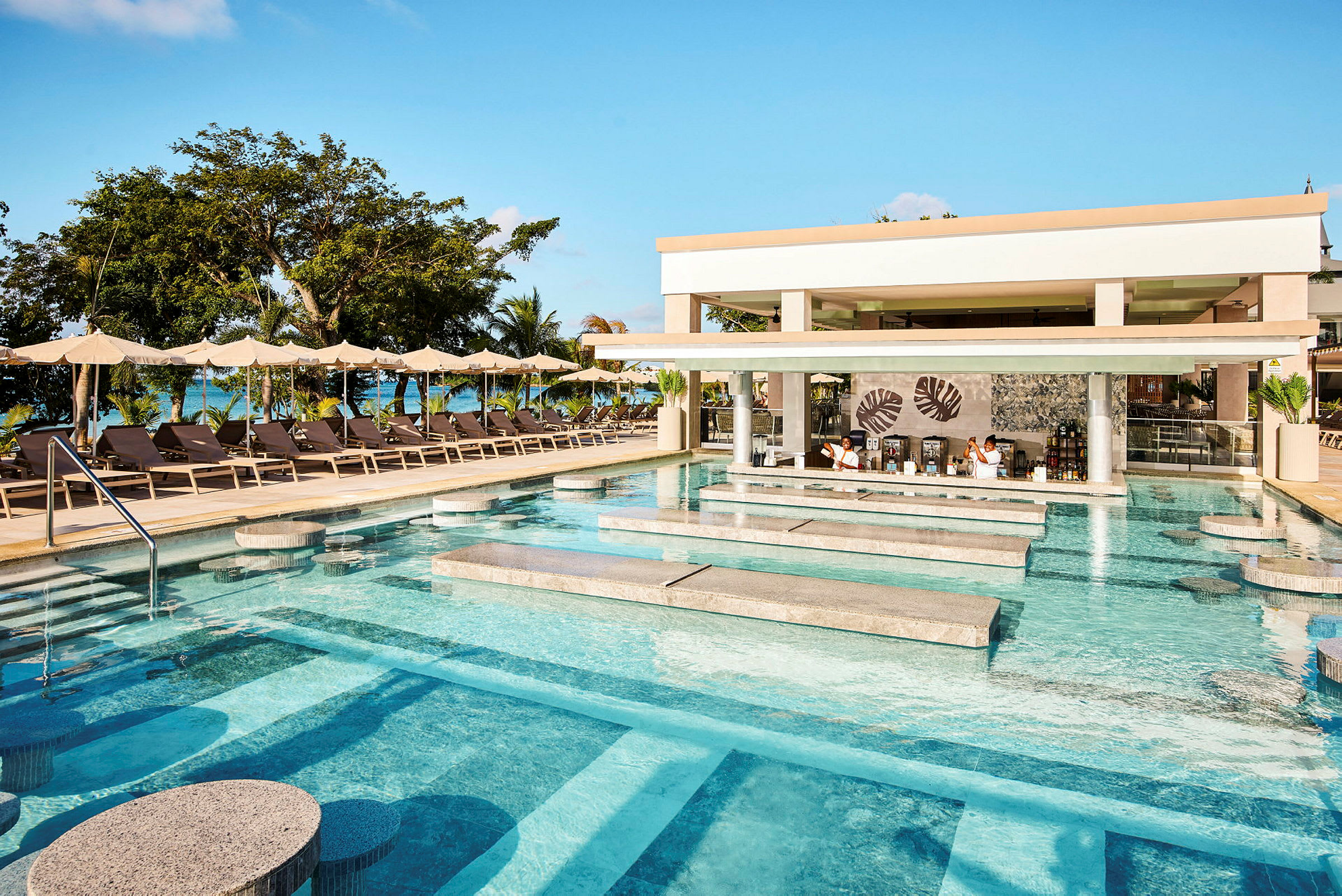 Et basseng med sitteplasser og en swim-up bar ved en resort med solsenger og parasoller i bakgrunnen. (AI-generert tekst)