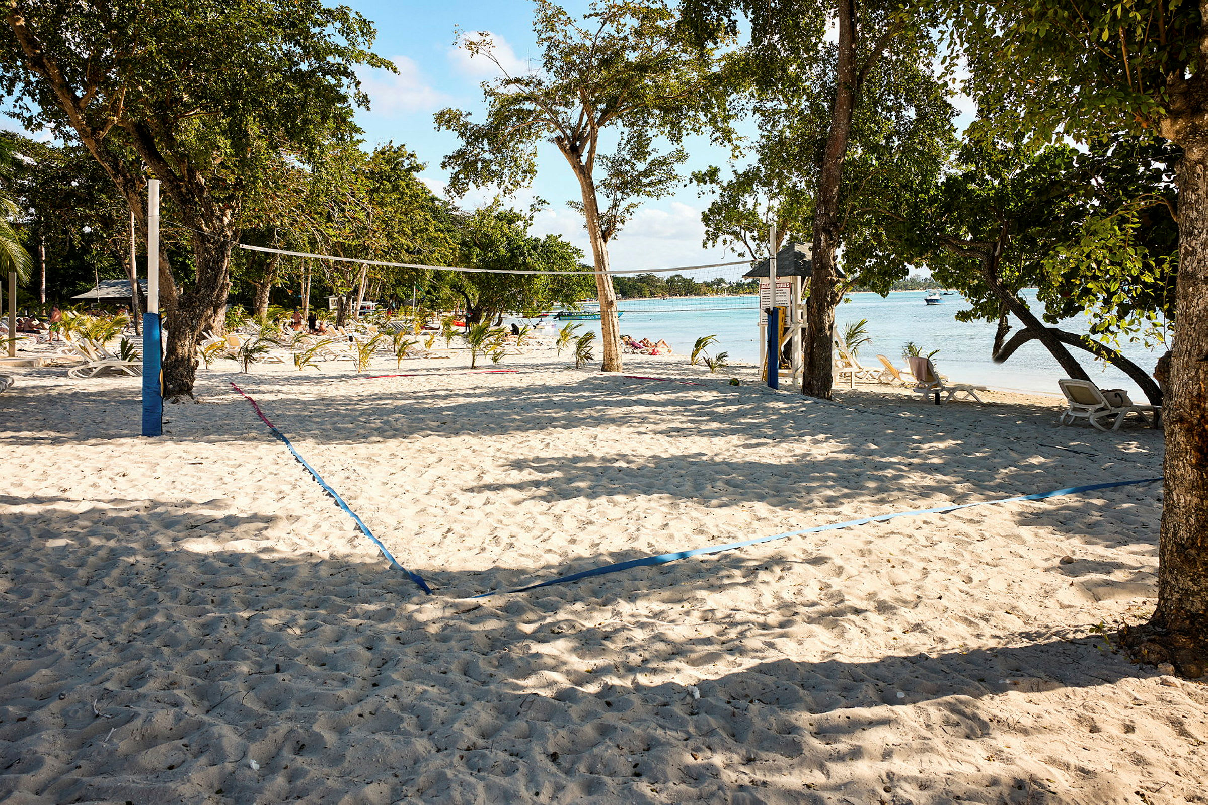 En sandstrand med volleyballnett og stoler i bakgrunnen. (AI-generert tekst)