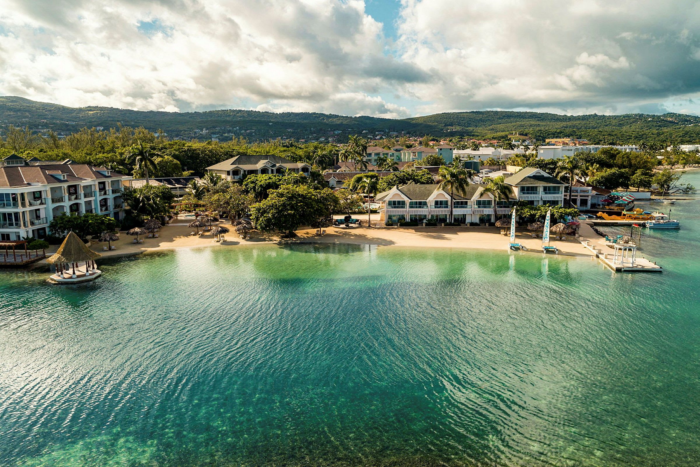 Luftfoto av en strand med hotellbygninger og grøntområder. (AI-generert tekst)