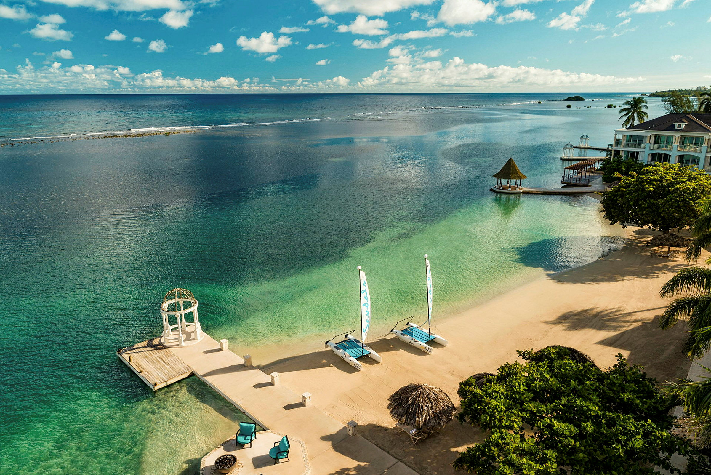 Strand med klart vann, solsenger og seilbåter. (AI-generert tekst)