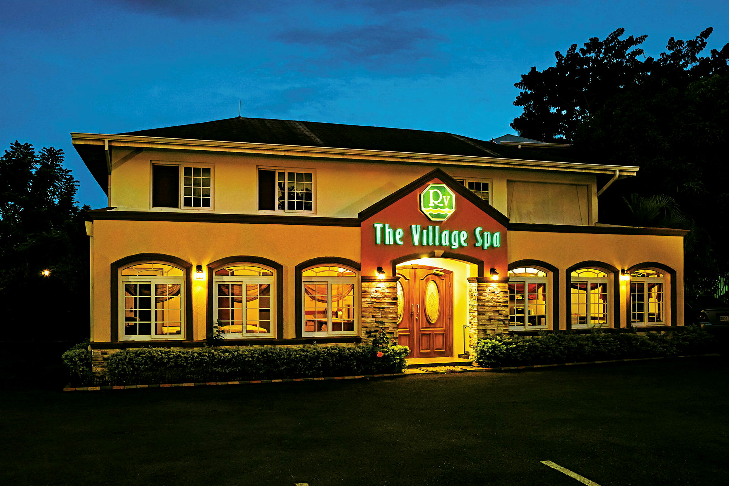 Bygning med to etasjer, opplyst fasade og inngang med et skilt som viser navnet "The Village Spa". (AI-generert tekst)