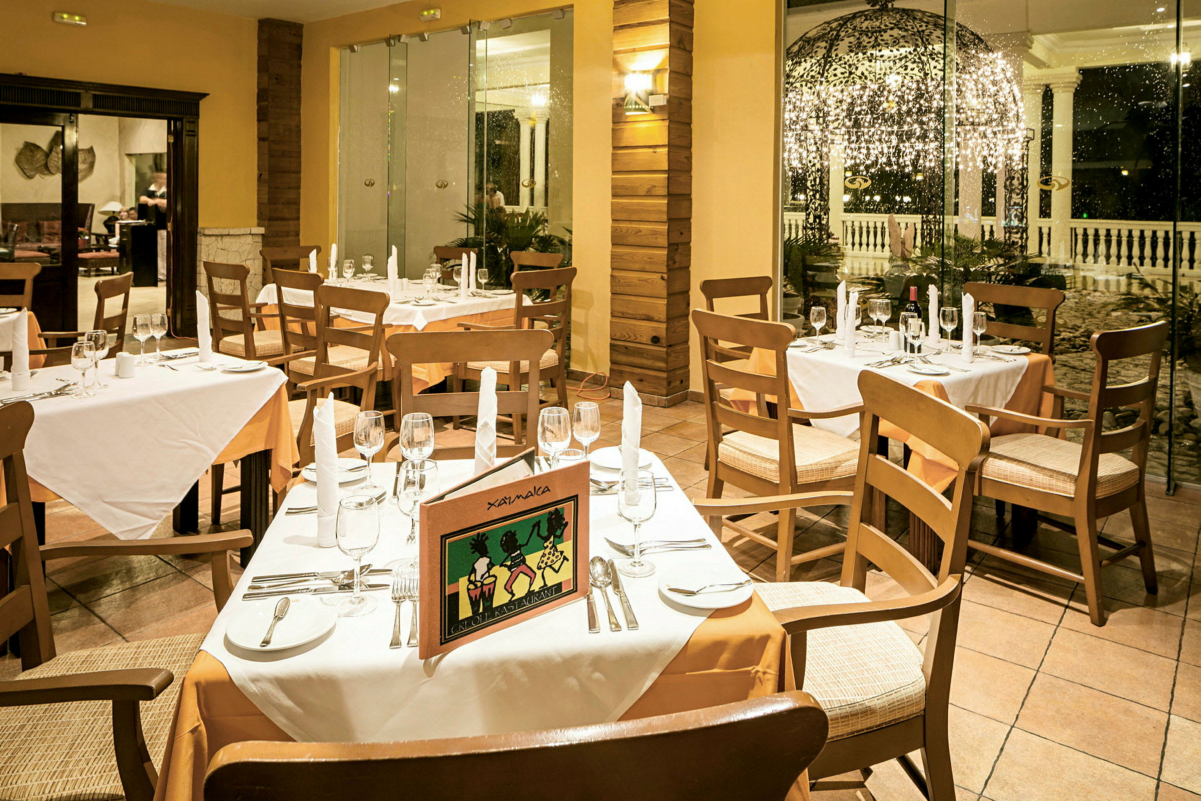 En restaurant med dekkede bord, hvite duker og trestoler, med et åpent område og dekorert uteområde i bakgrunnen. (AI-generert tekst)