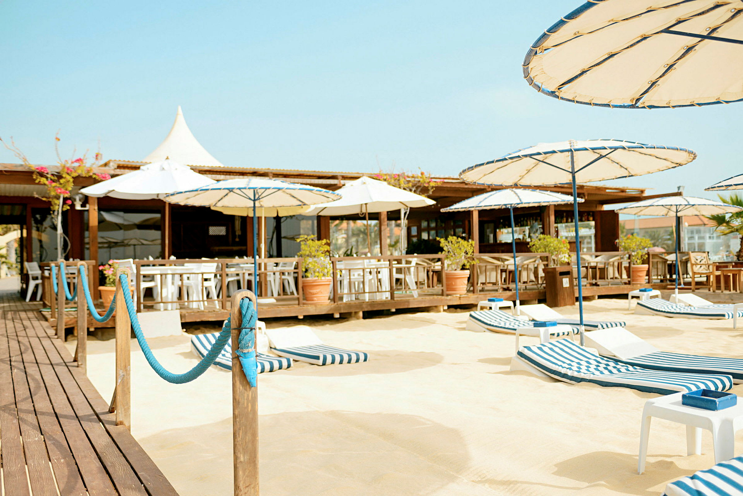 En strandbar med sitteplasser, parasoller og solsenger på en sandflate. (AI-generert tekst)