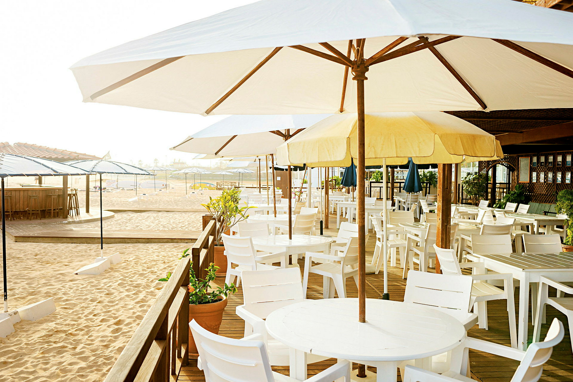 En strandbar med parasoller og hvite bord og stoler. (AI-generert tekst)