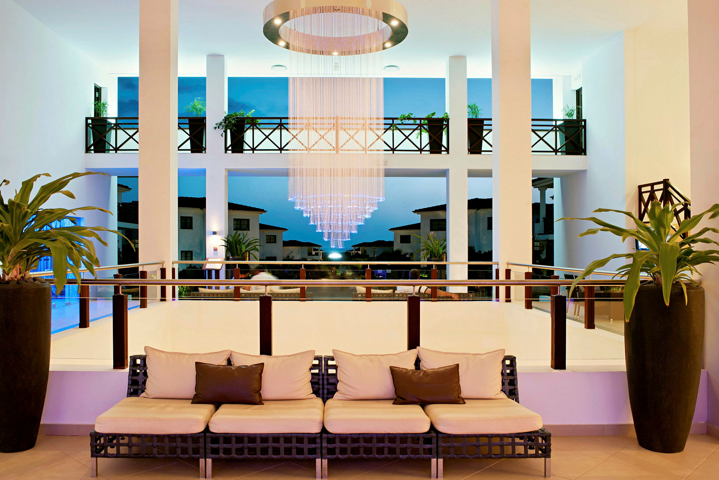 En hotellobby med sofa, hengende lysekrone og utsikt mot uteområde. (AI-generert tekst)