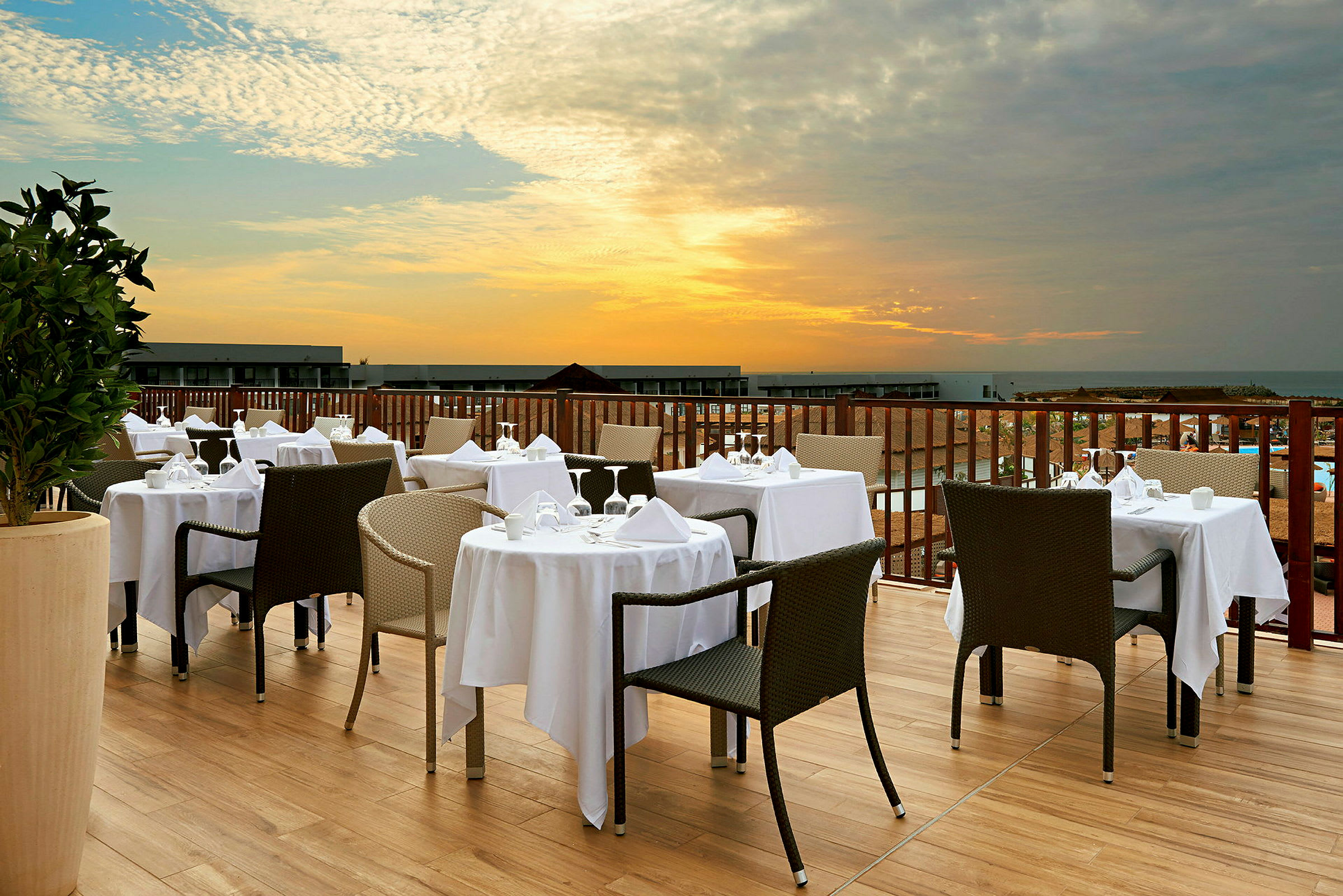 En terrasse med dekte bord og stoler med utsikt over solnedgangen. (AI-generert tekst)
