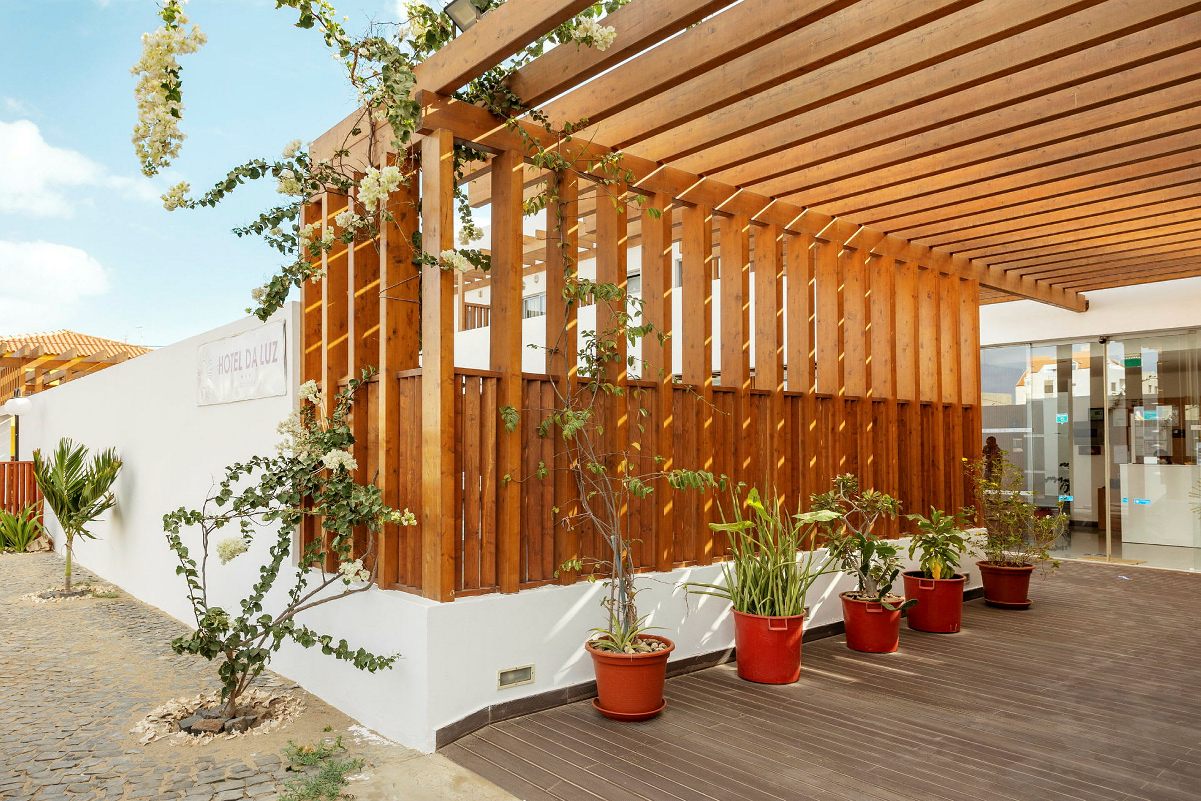 Trepergola med klatreplanter og potteplanter ved en bygning. (AI-generert tekst)