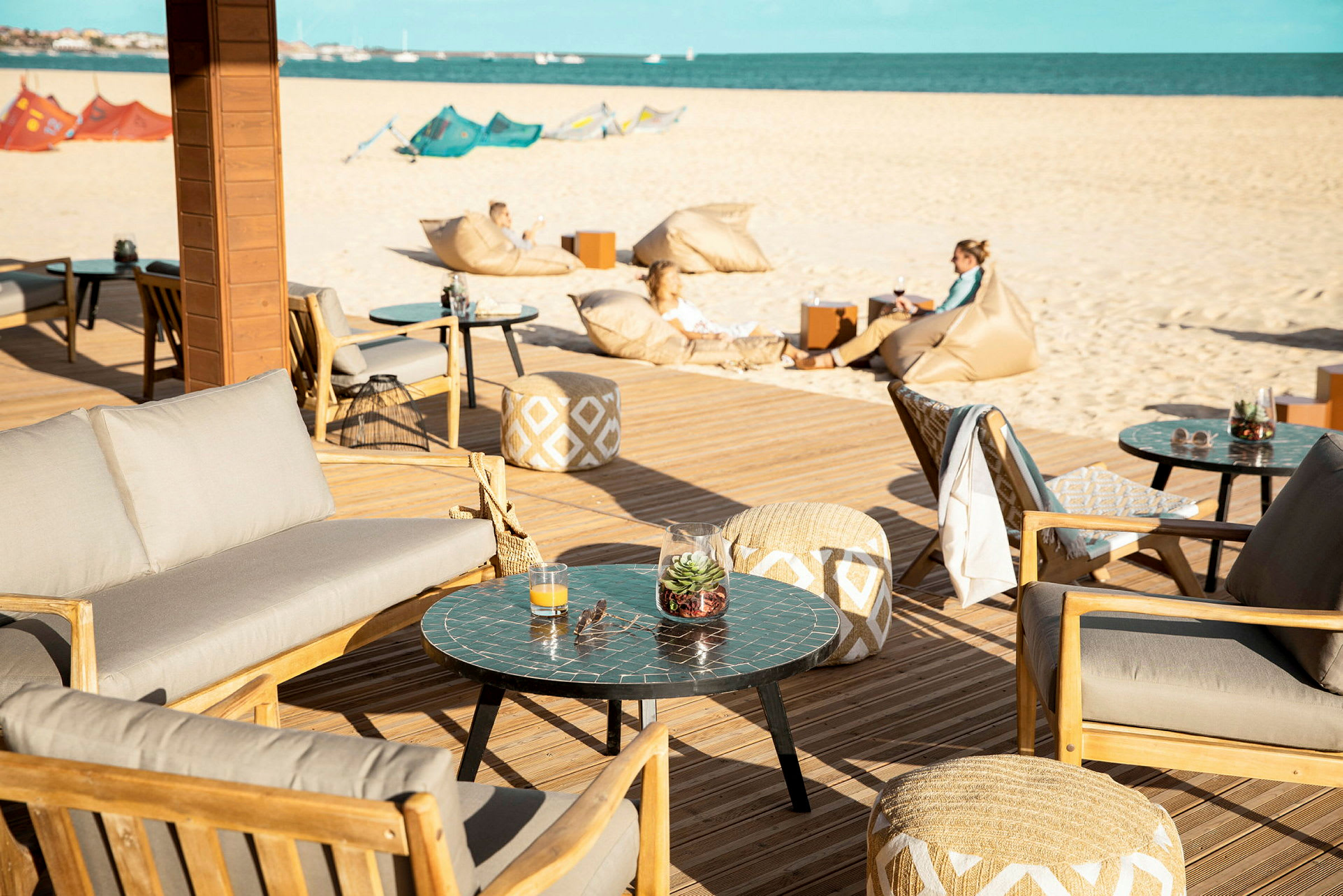 Terrasse med sittemøbler og bord, i bakgrunnen en sandstrand og havet. (AI-generert tekst)