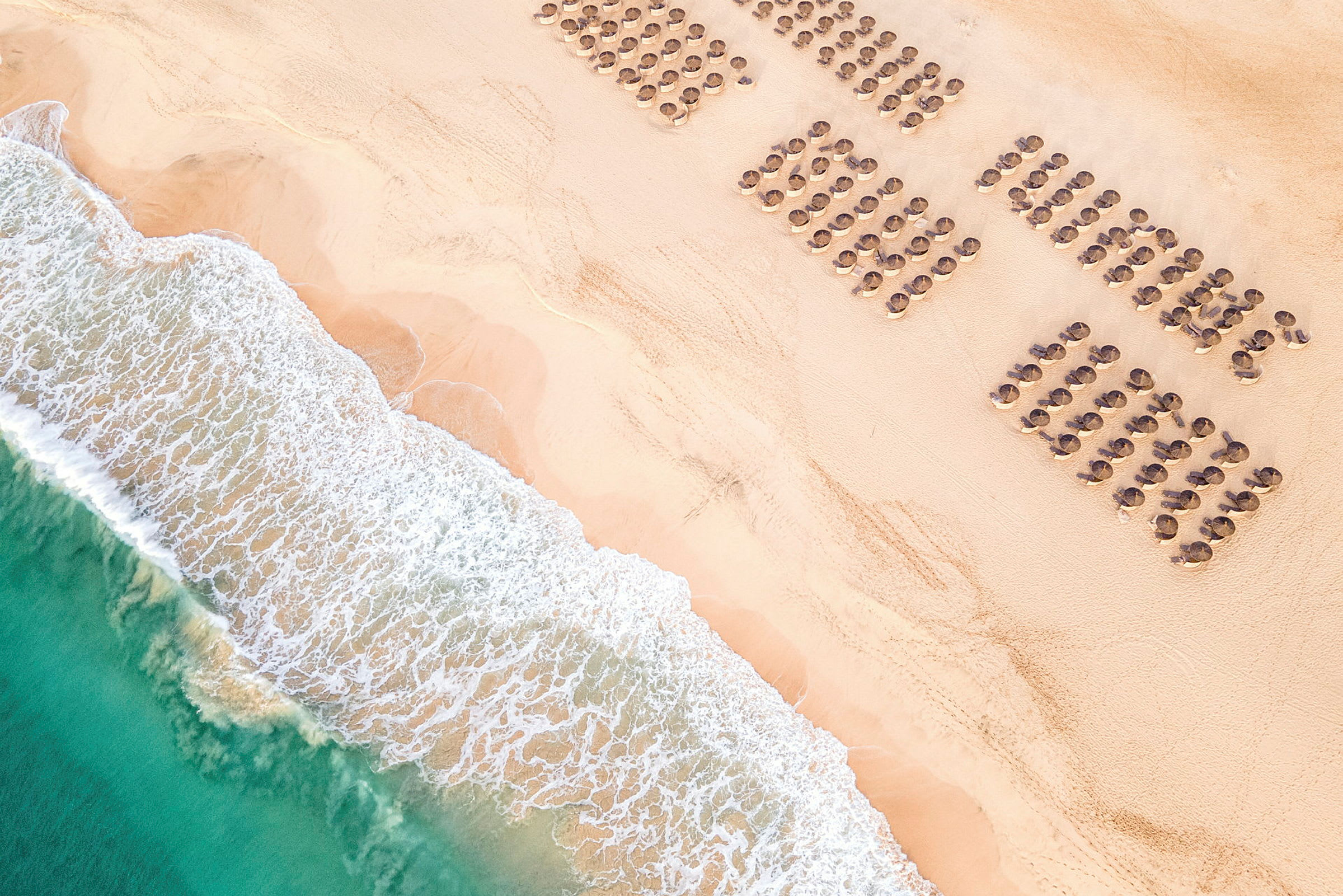 Luftfoto av en strand med parasoller på rad og bølger som skyller in. (AI-generert tekst)