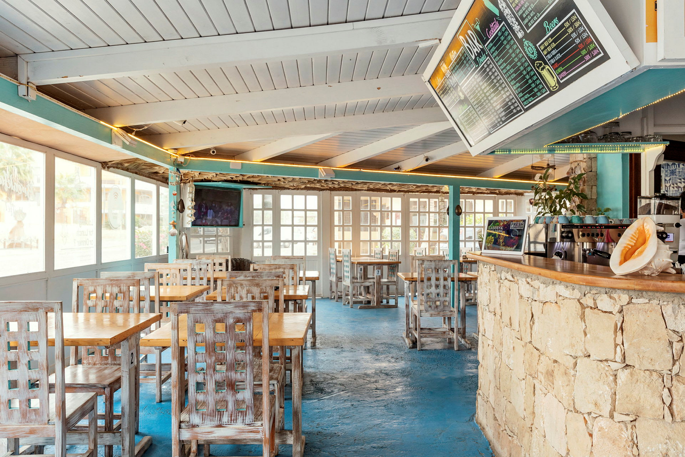 Interiør av en restaurant med trebord og stoler, blått gulv og en meny på veggen. (AI-generert tekst)