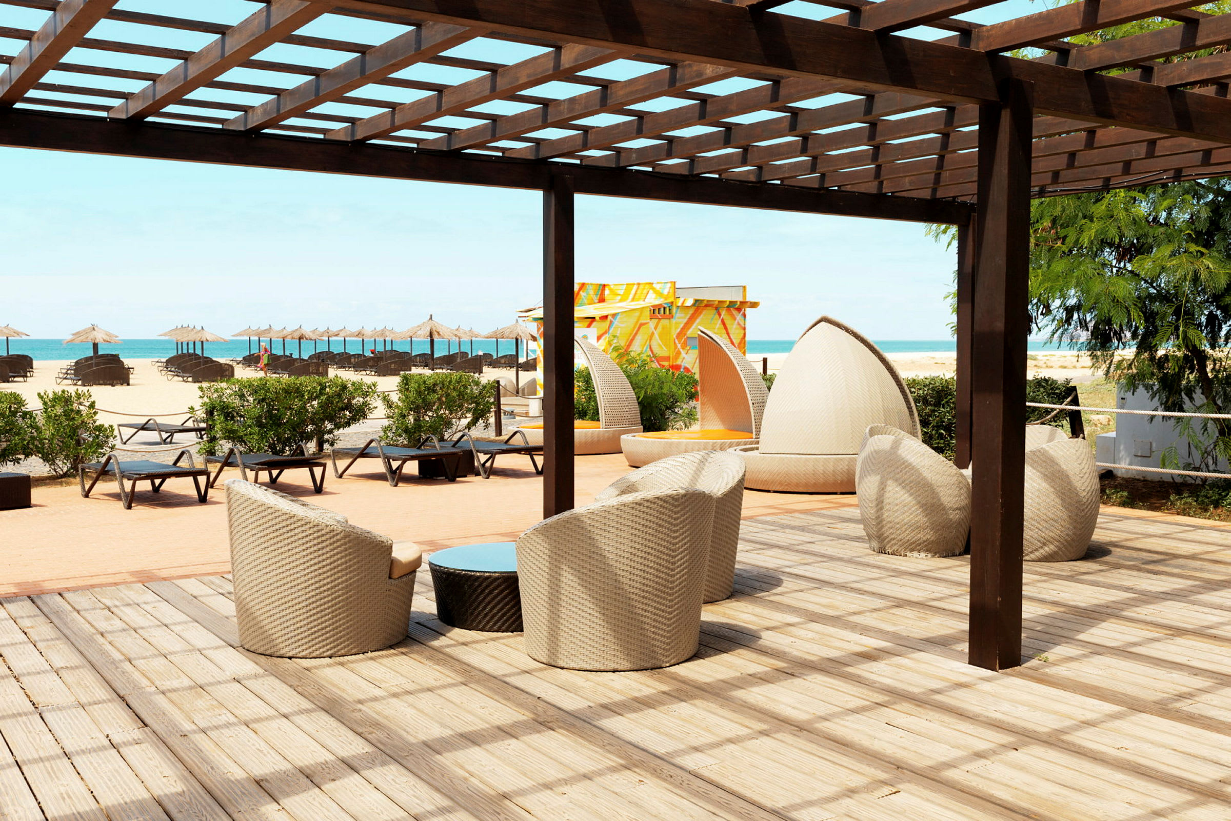 Loungeområde med sittemøbler under en pergola nær stranden. (AI-generert tekst)