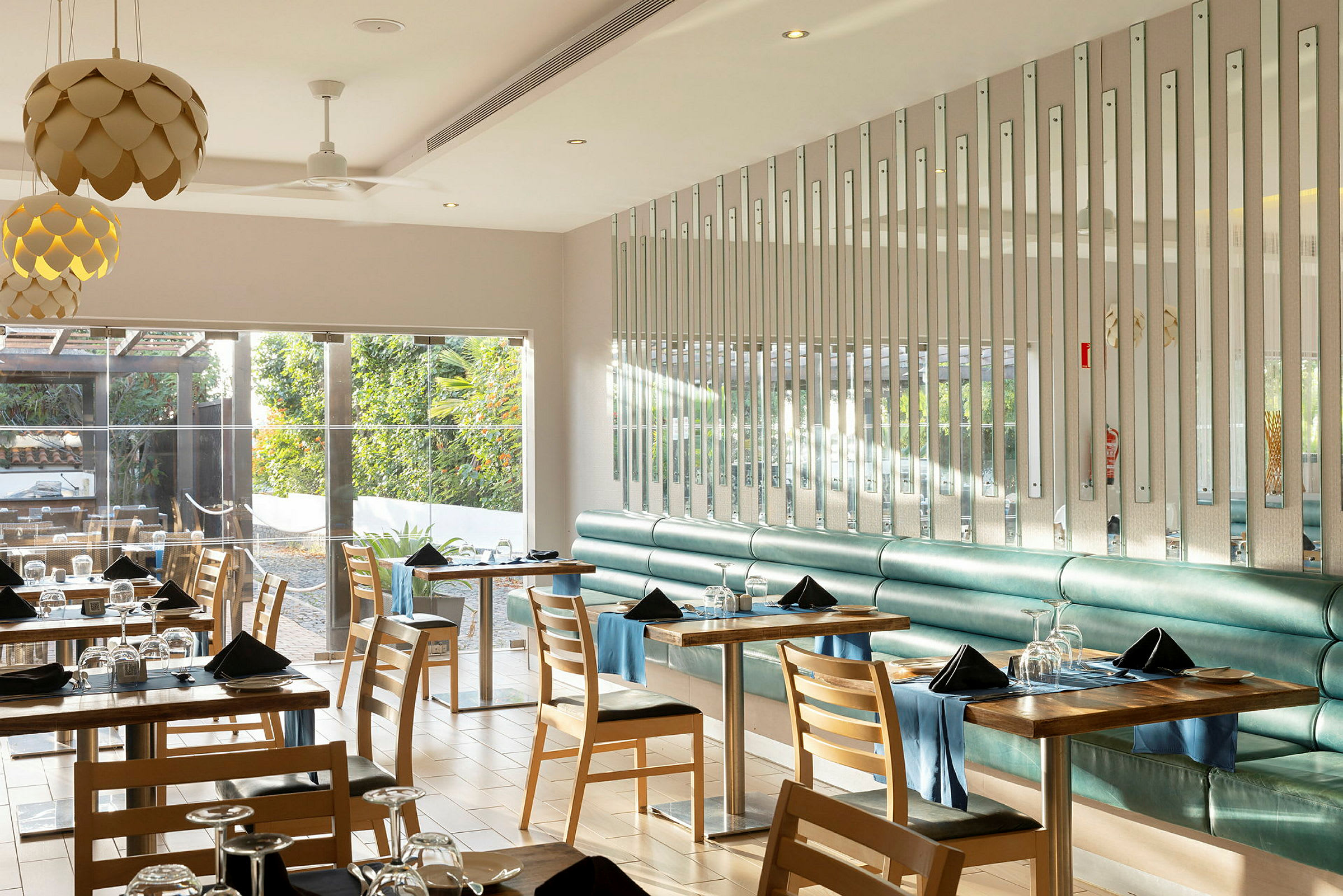 En moderne og lys restaurantinteriør med bord og stoler, hvor vinduer vender mot et frodig utendørsområde. (AI-generert tekst)