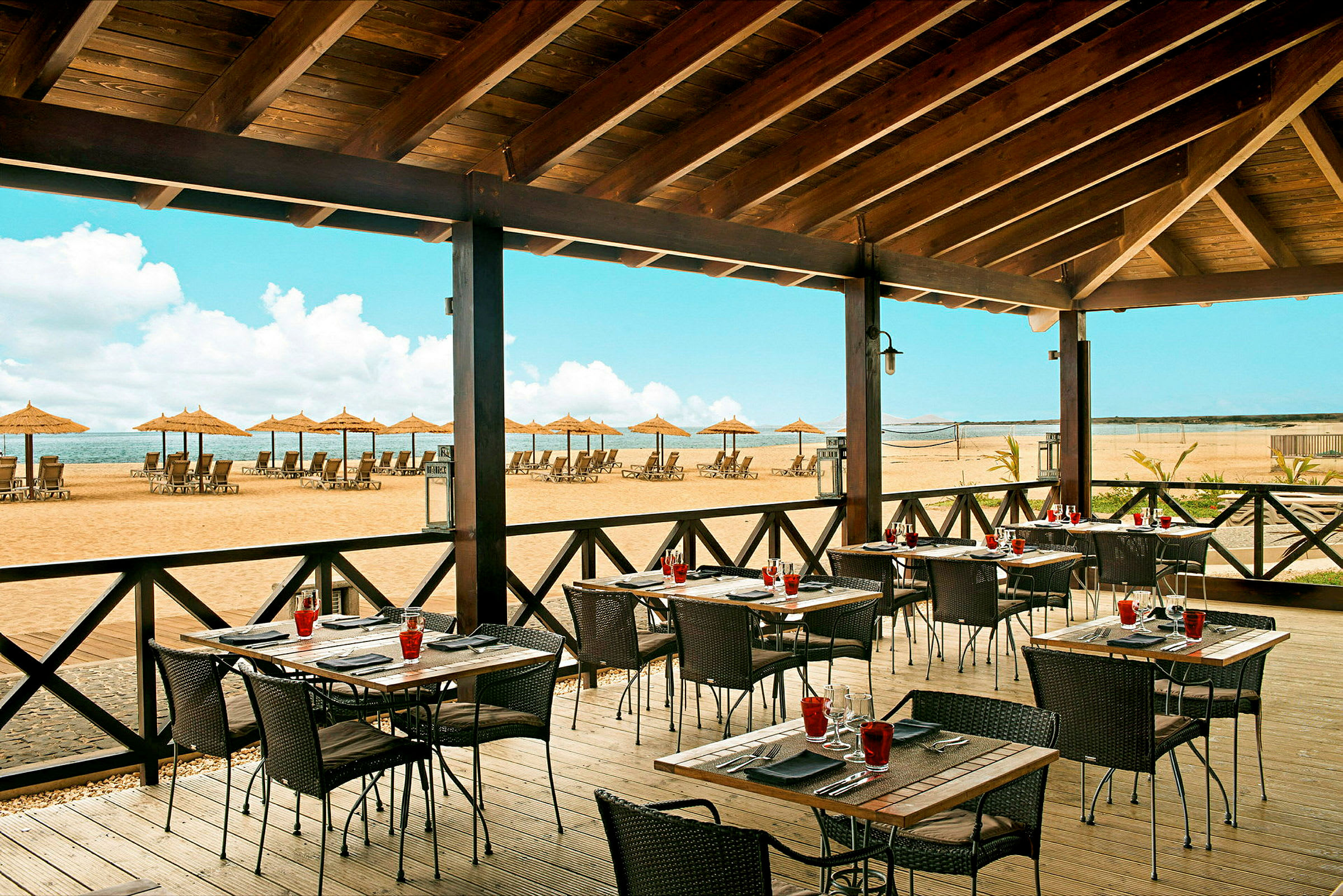 Restaurant med uteservering og utsikt over en strand med solsenger og parasoller. (AI-generert tekst)