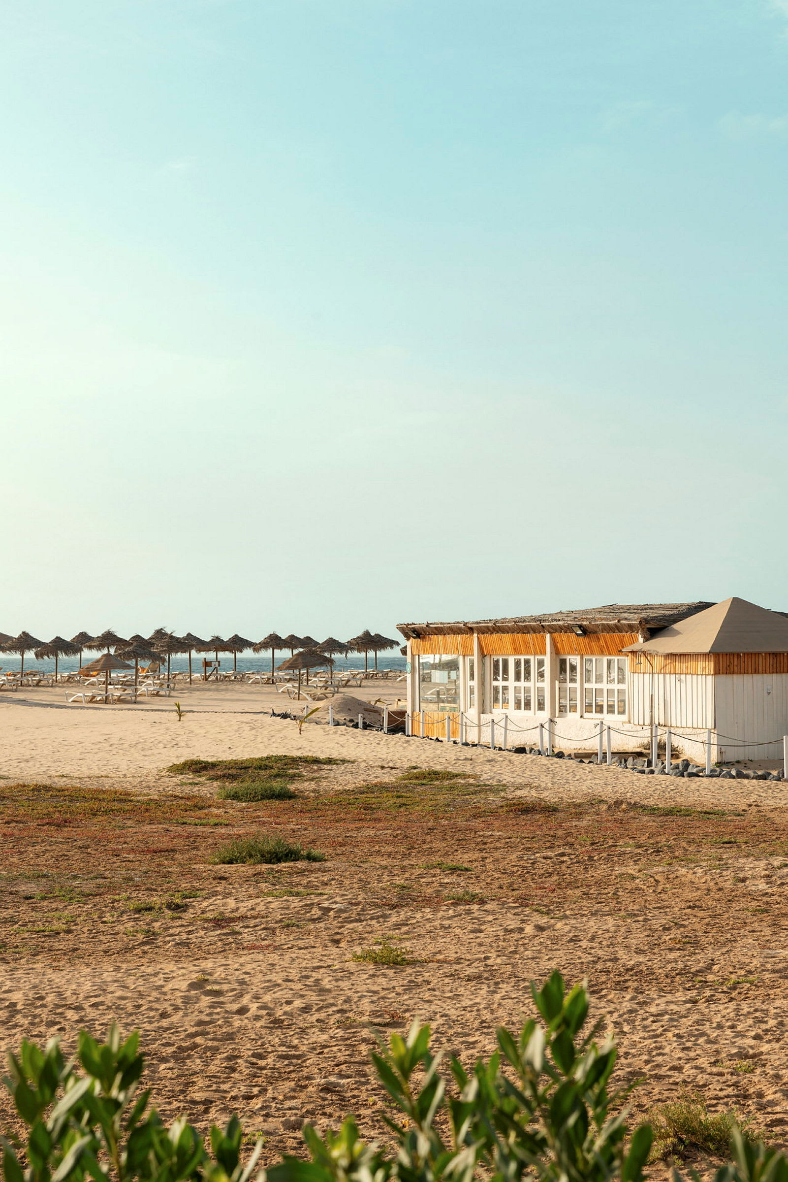 Strand med parasoller og en trebygning. (AI-generert tekst)