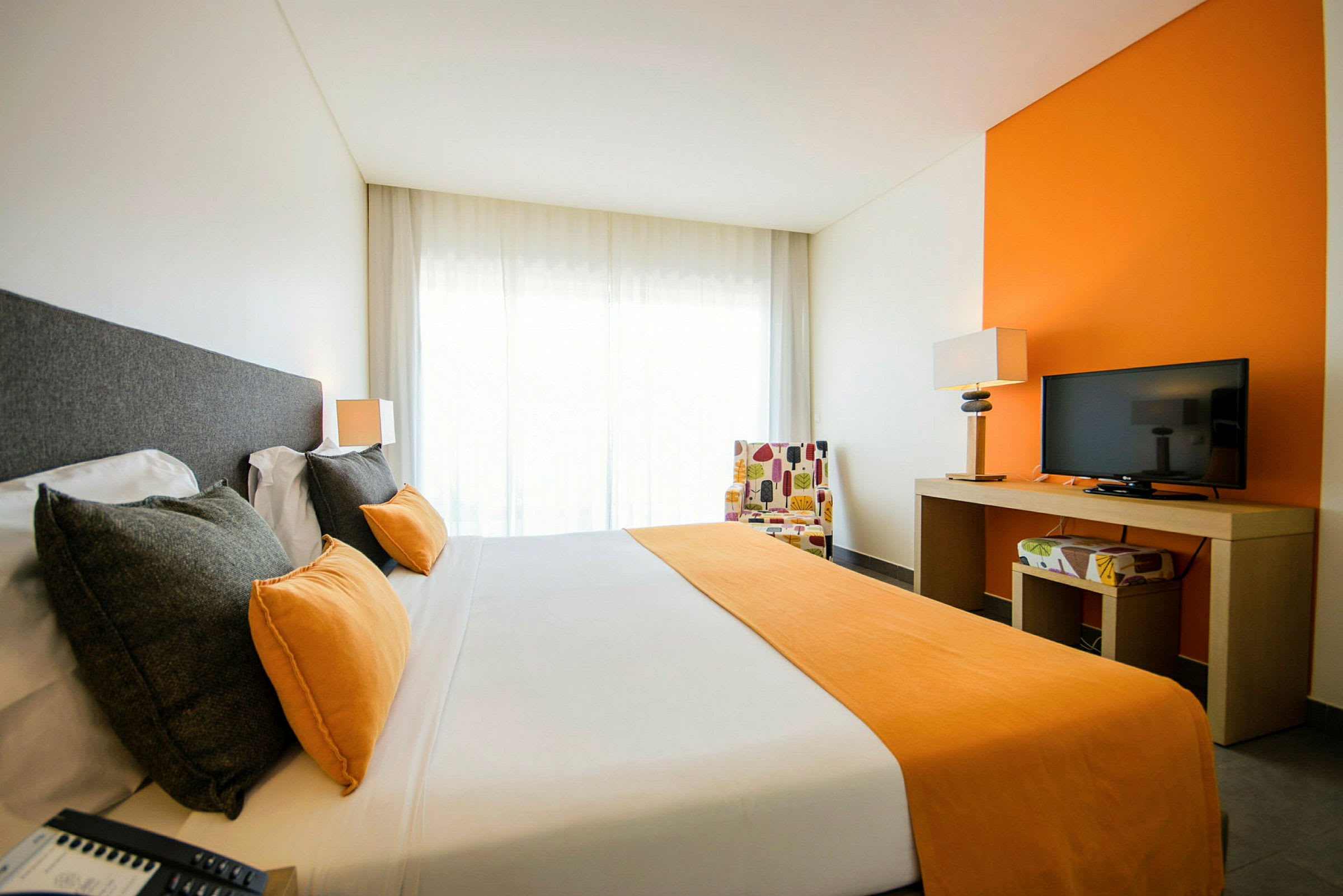 Bilde av et hotellrom med en dobbeltseng, orange detaljer og en TV på et bord. (AI-generert tekst)