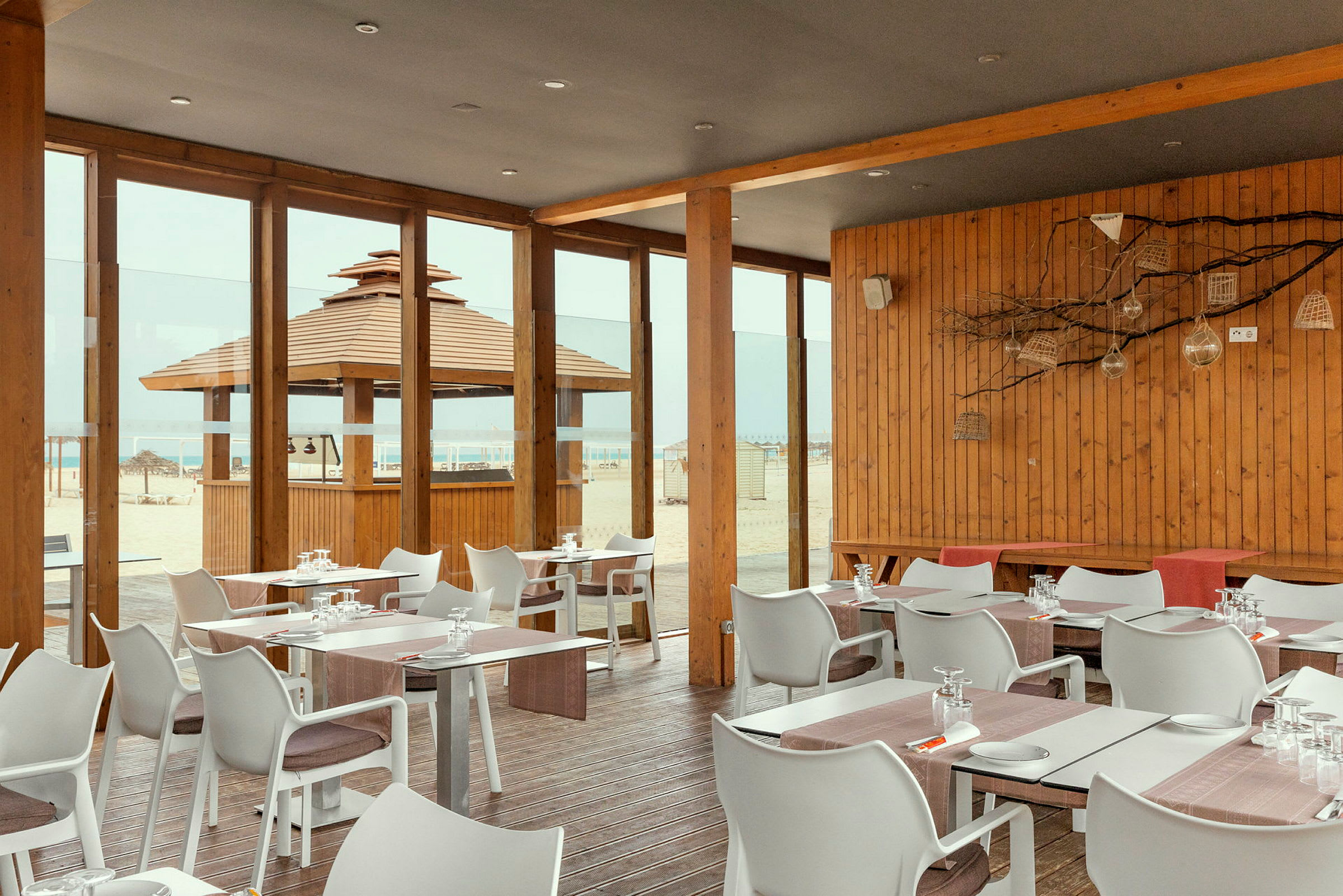 Restaurant med trepanel og glassvegger med utsikt over stranden. (AI-generert tekst)