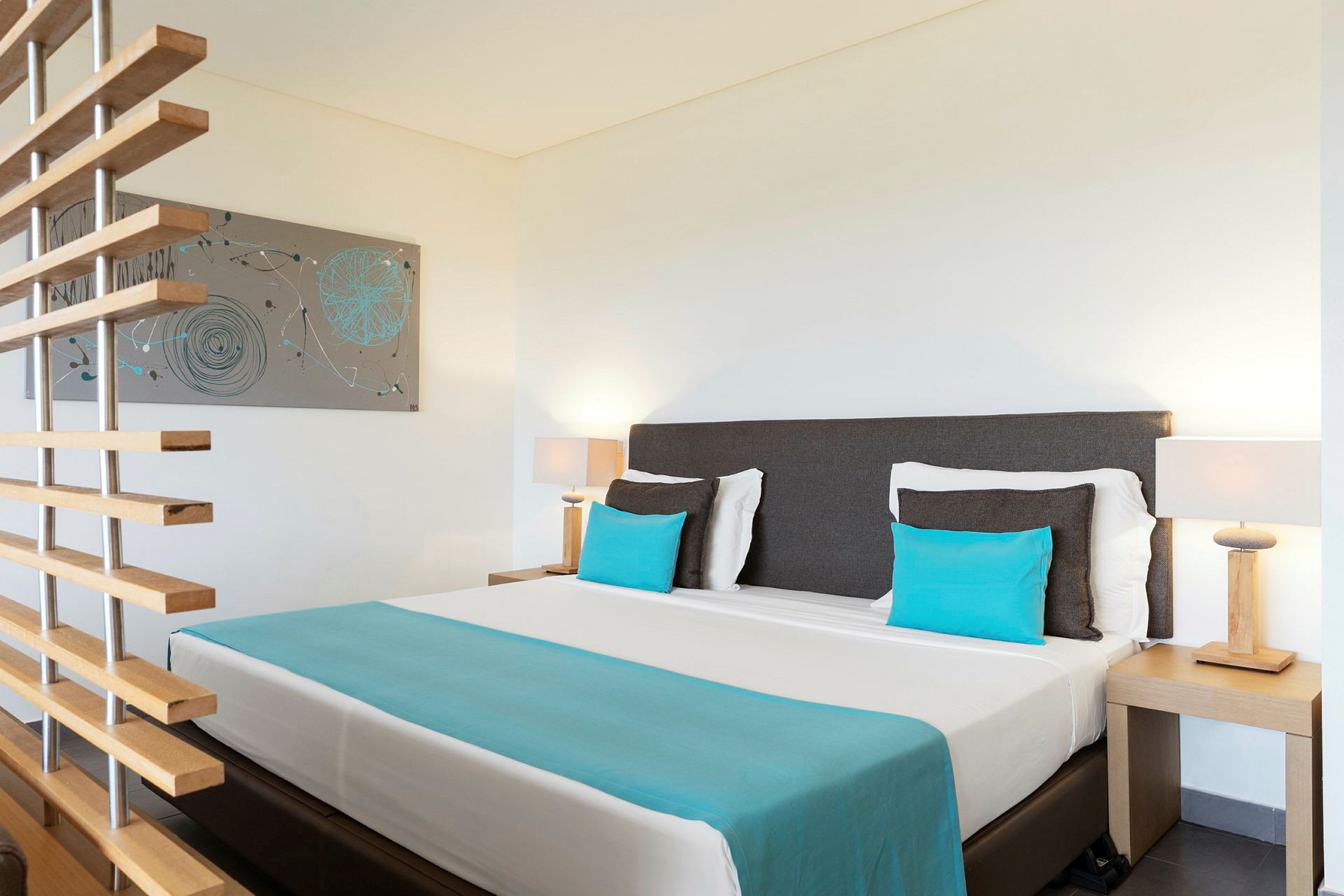 Et hotellrom med en seng og blå puter samt en veggdekorasjon. (AI-generert tekst)