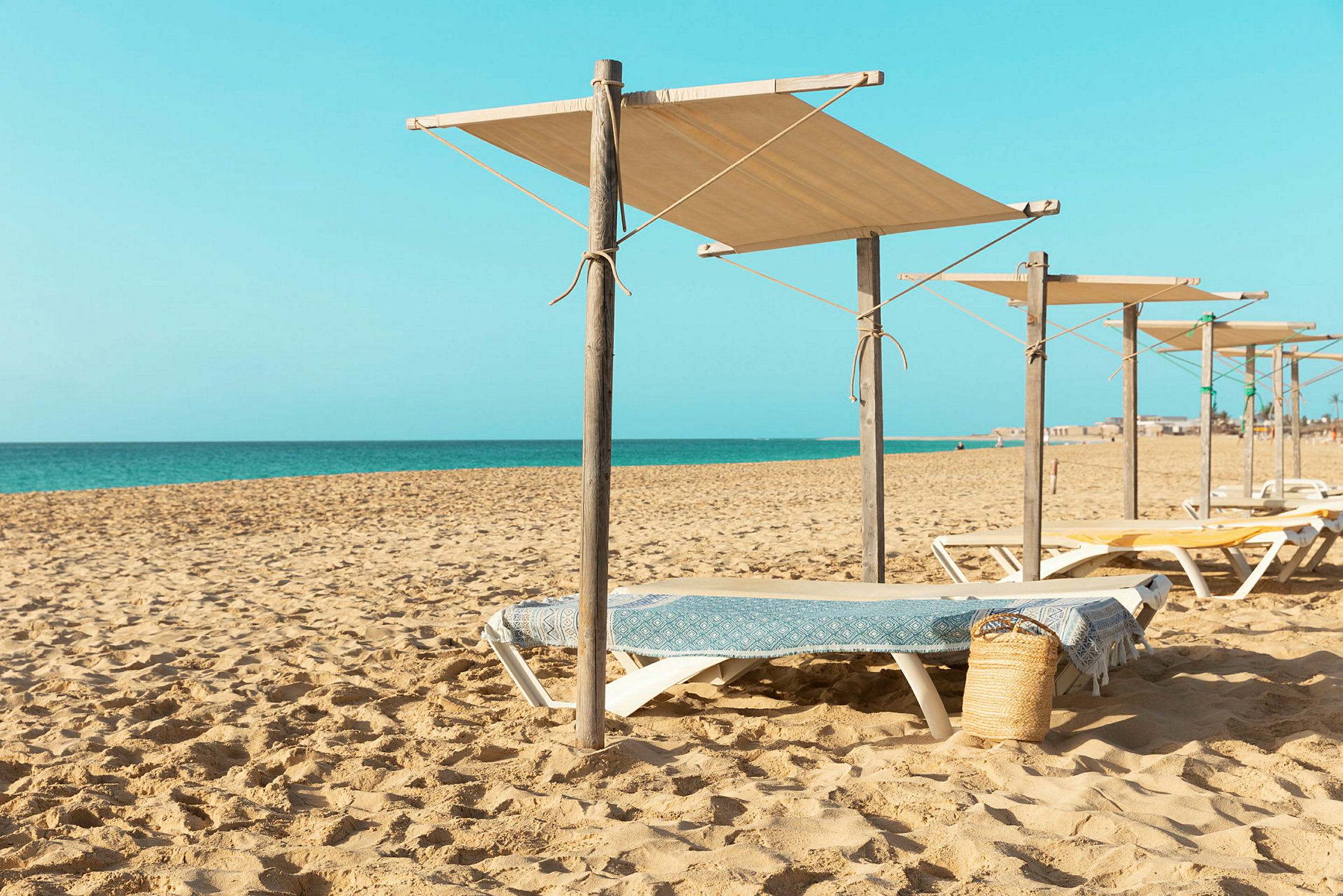 Solstoler med skyggefulle parasoller på en sandstrand med havet i bakgrunnen. (AI-generert tekst)