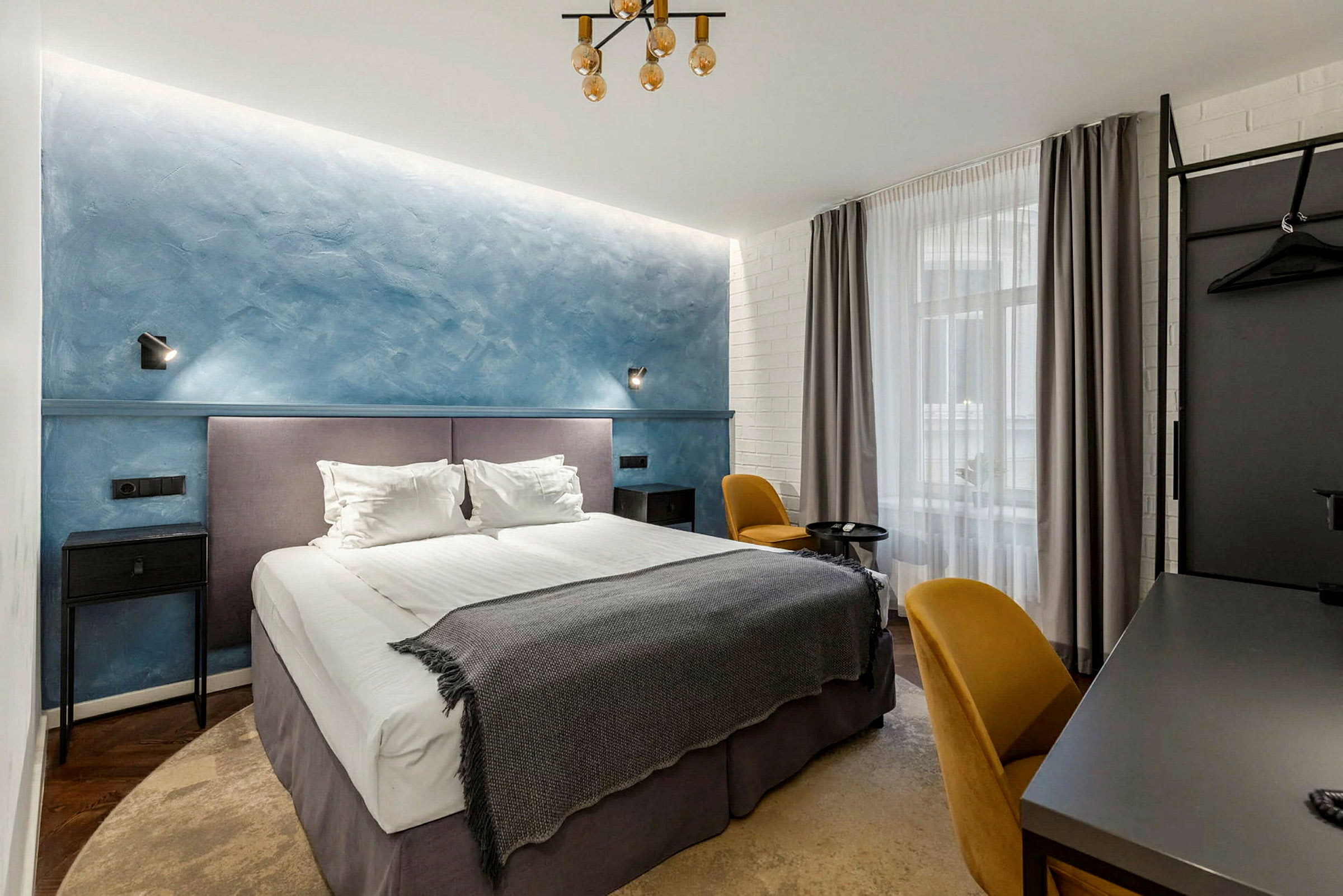 Et hotellrom med en dobbeltseng, blå vegg og gule stoler. (AI-generert tekst)