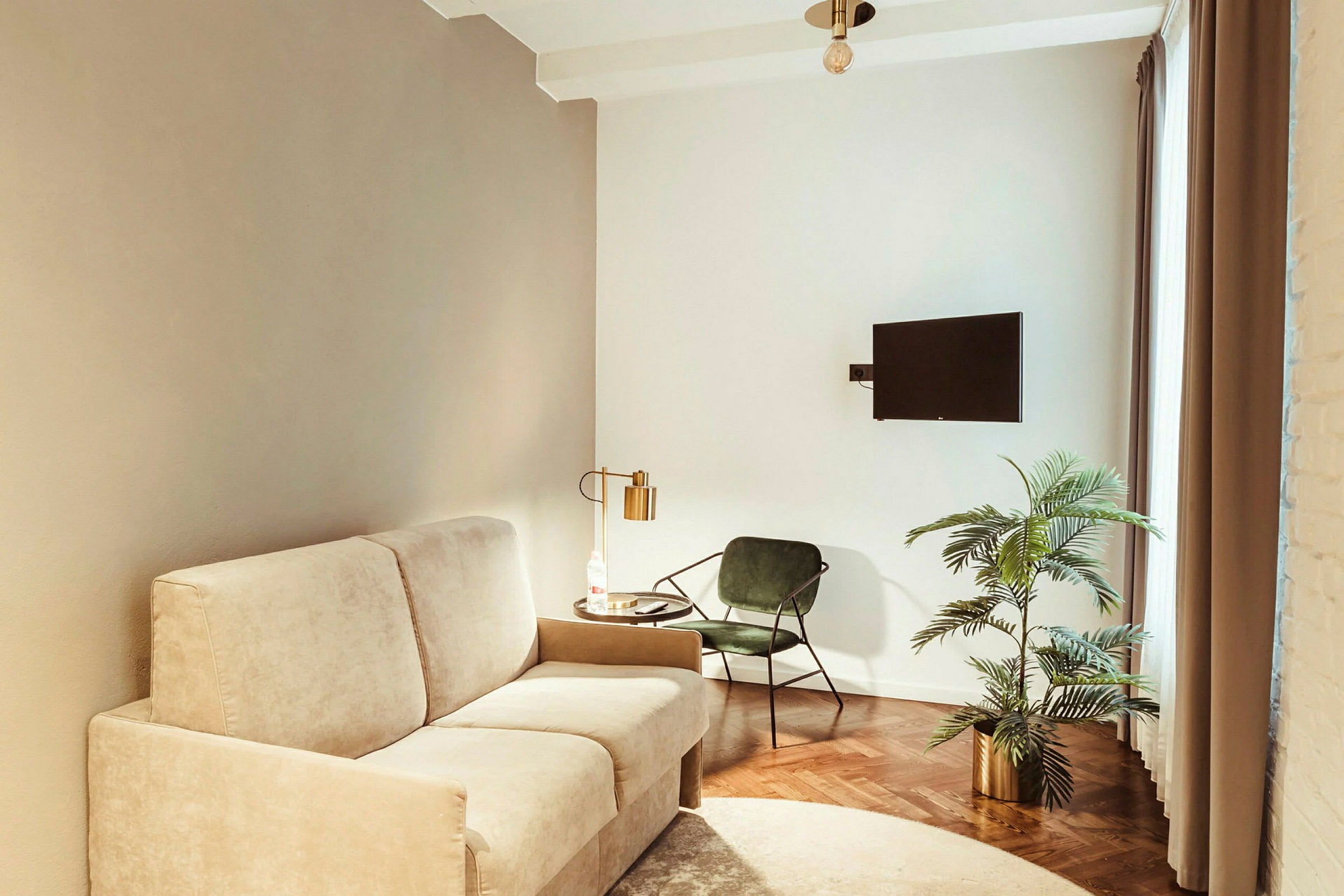 Et stue med beige sofa, grønn stol, bord med lampe, plante i potte og vægghengt TV. (AI-generert tekst)