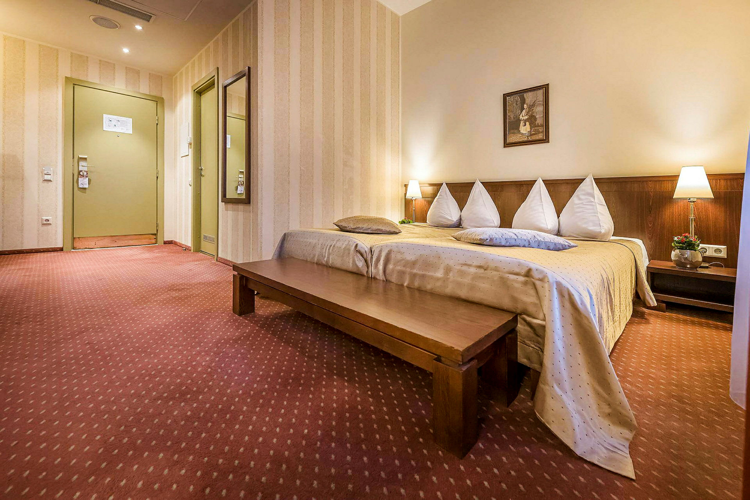 Et hotellrom med en oppredd seng, en lang trebenk og dekorative lamper. (AI-generert tekst)