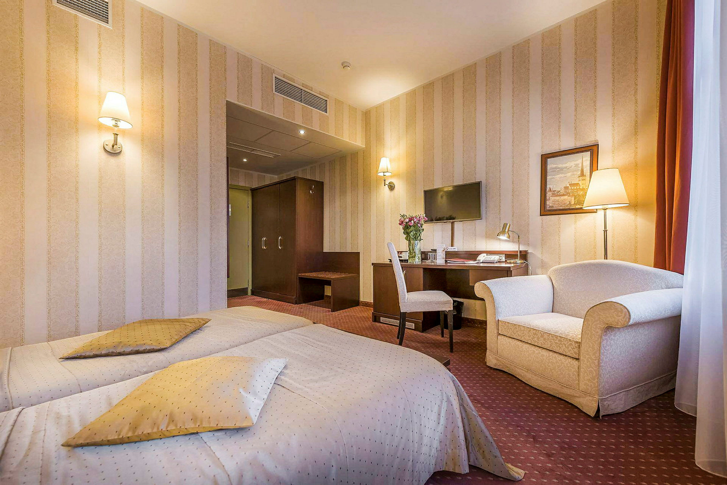 Hotellrom med to enkeltsenger, skrivebord med stol, TV på veggen og en lenestol. (AI-generert tekst)