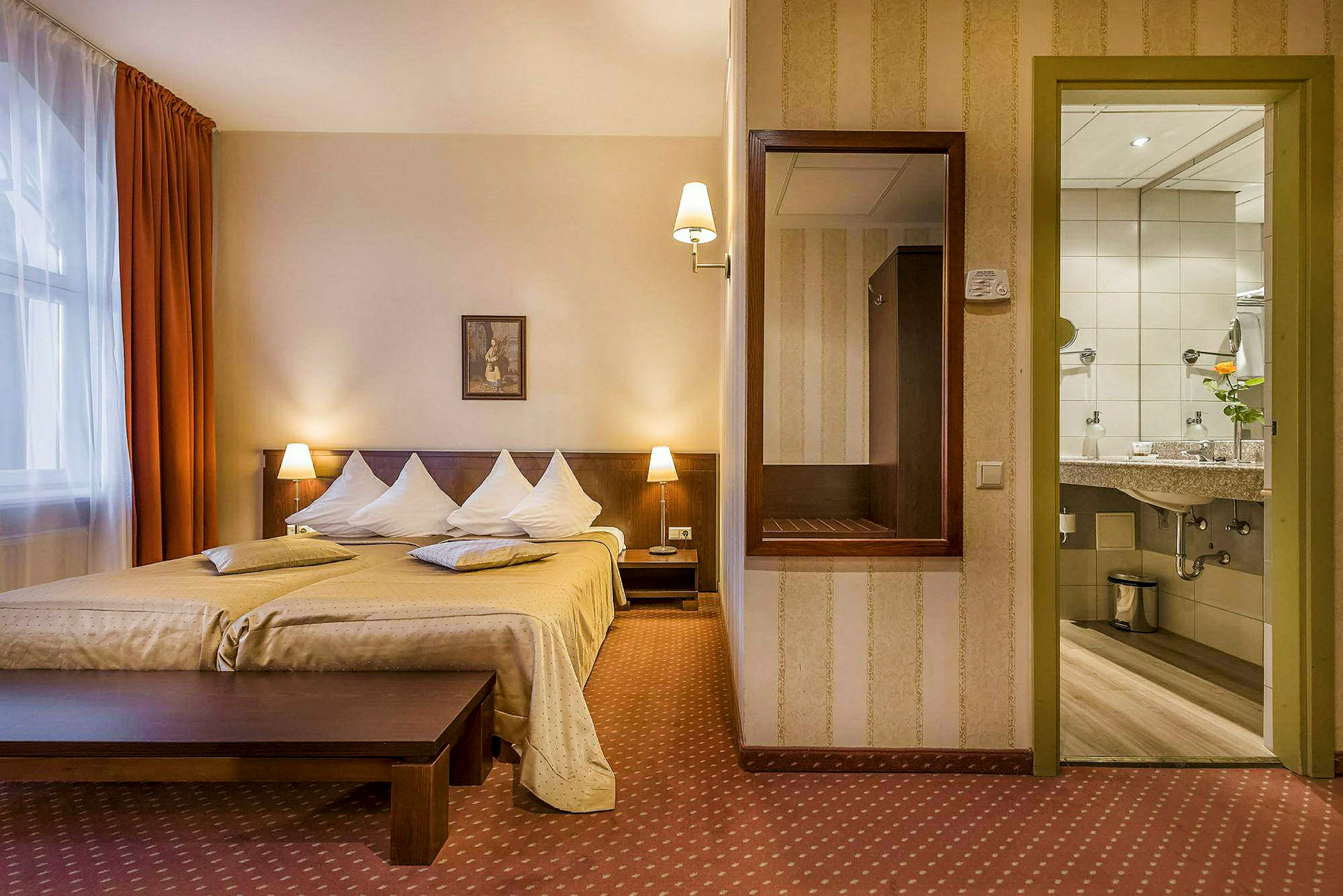 Et hotellrom med en dobbeltseng, to nattbord med lamper, et speil på veggen og utsikt mot badet. (AI-generert tekst)