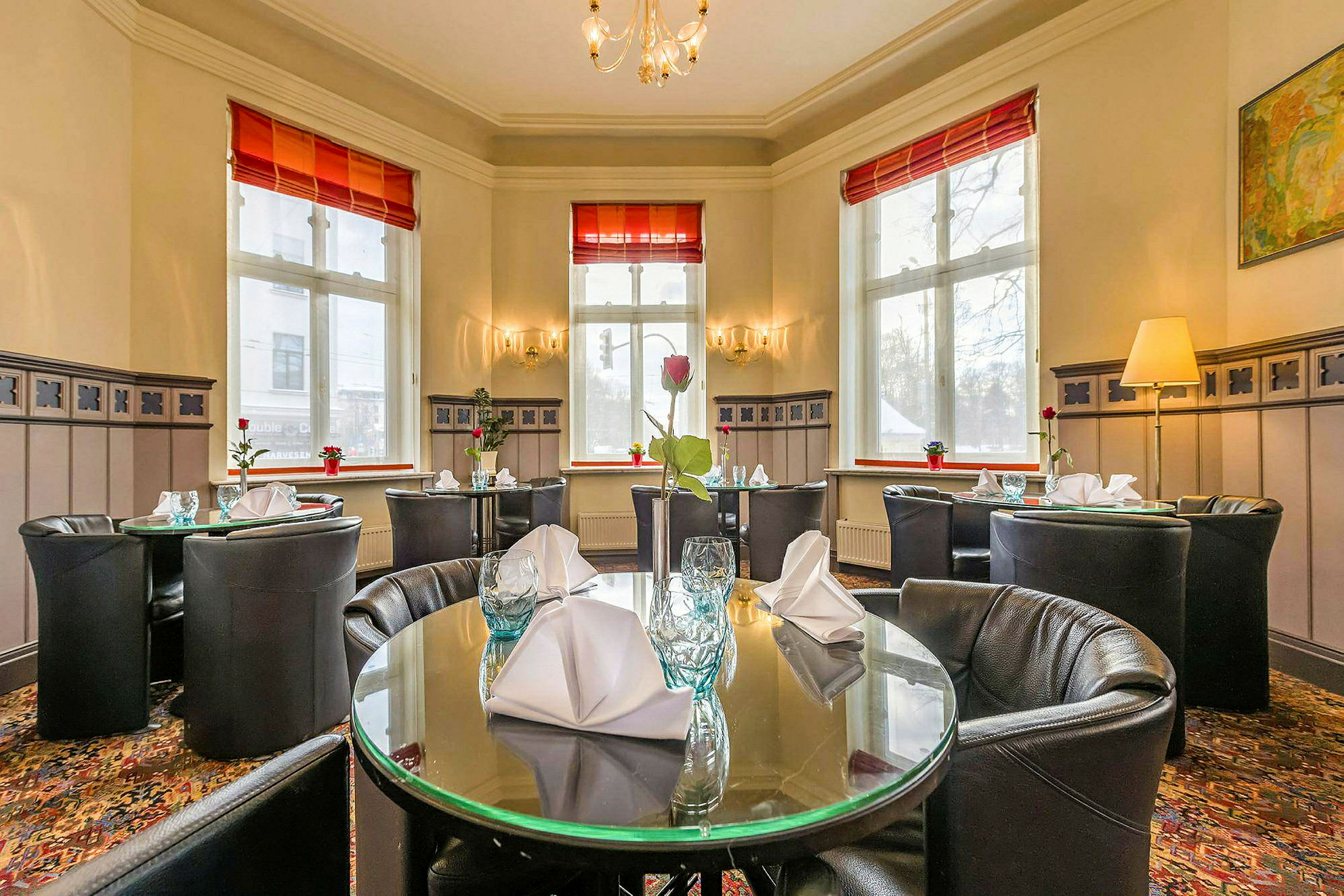 Interiør av en restaurant med dekkede, runde bord og store vinduer. (AI-generert tekst)