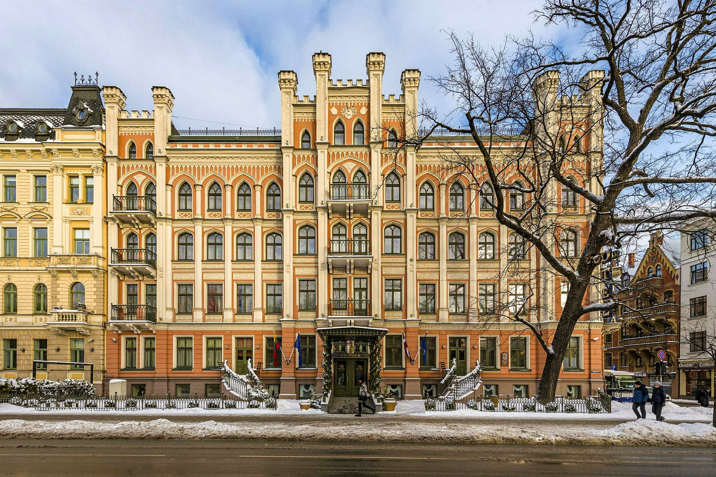 Fasaden til en staselig bygning med gotisk arkitektur og mange vinduer, sett på vinterstid med snø på bakken. (AI-generert tekst)