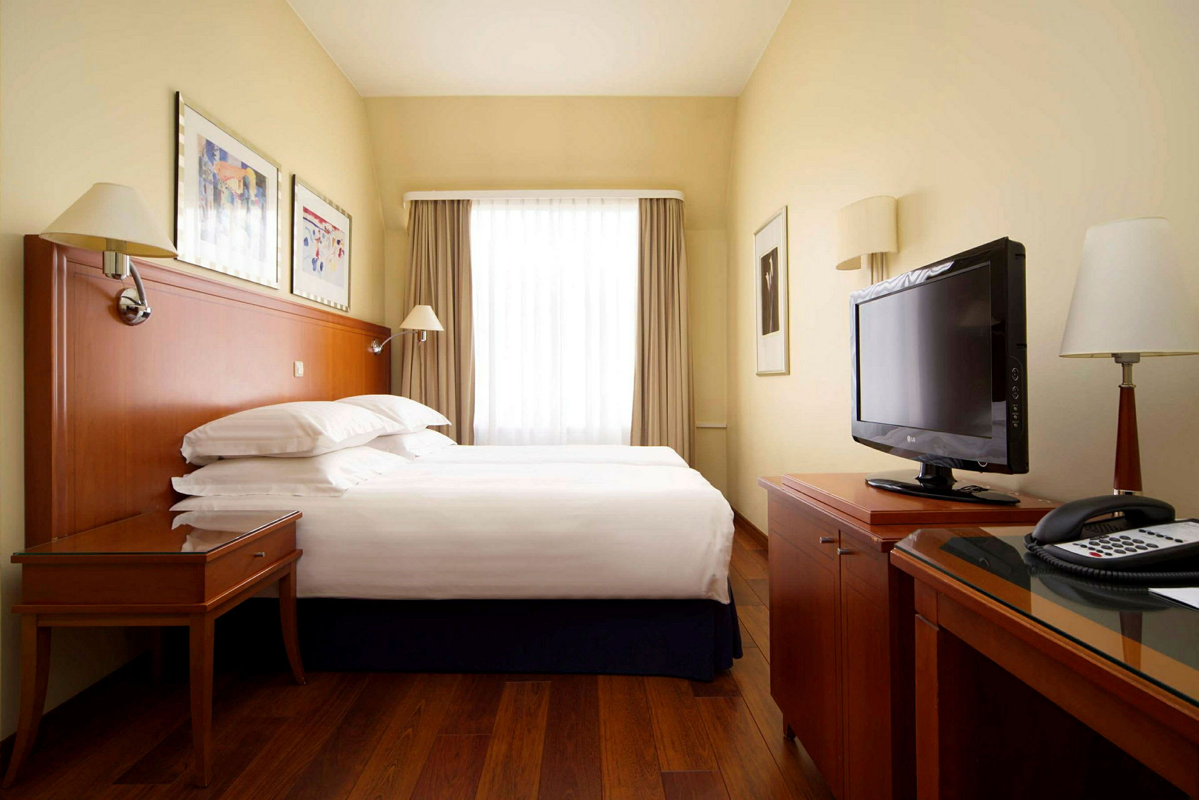 Hotellrom med en dobbeltseng, skrivebord, TV og store vinduer med gardiner. (AI-generert tekst)