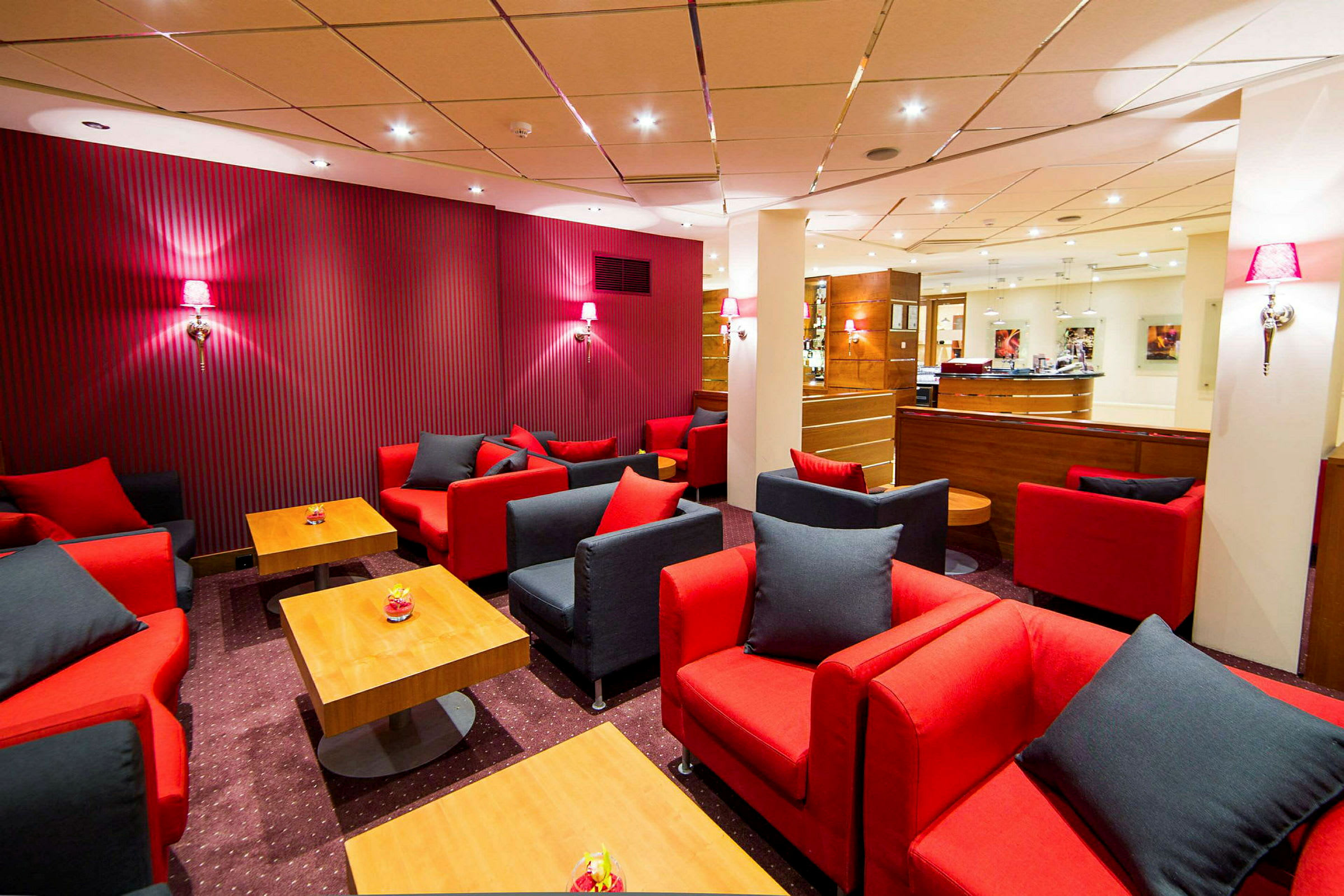 En elegant lounge med røde og svarte sofaer samt små bord. (AI-generert tekst)