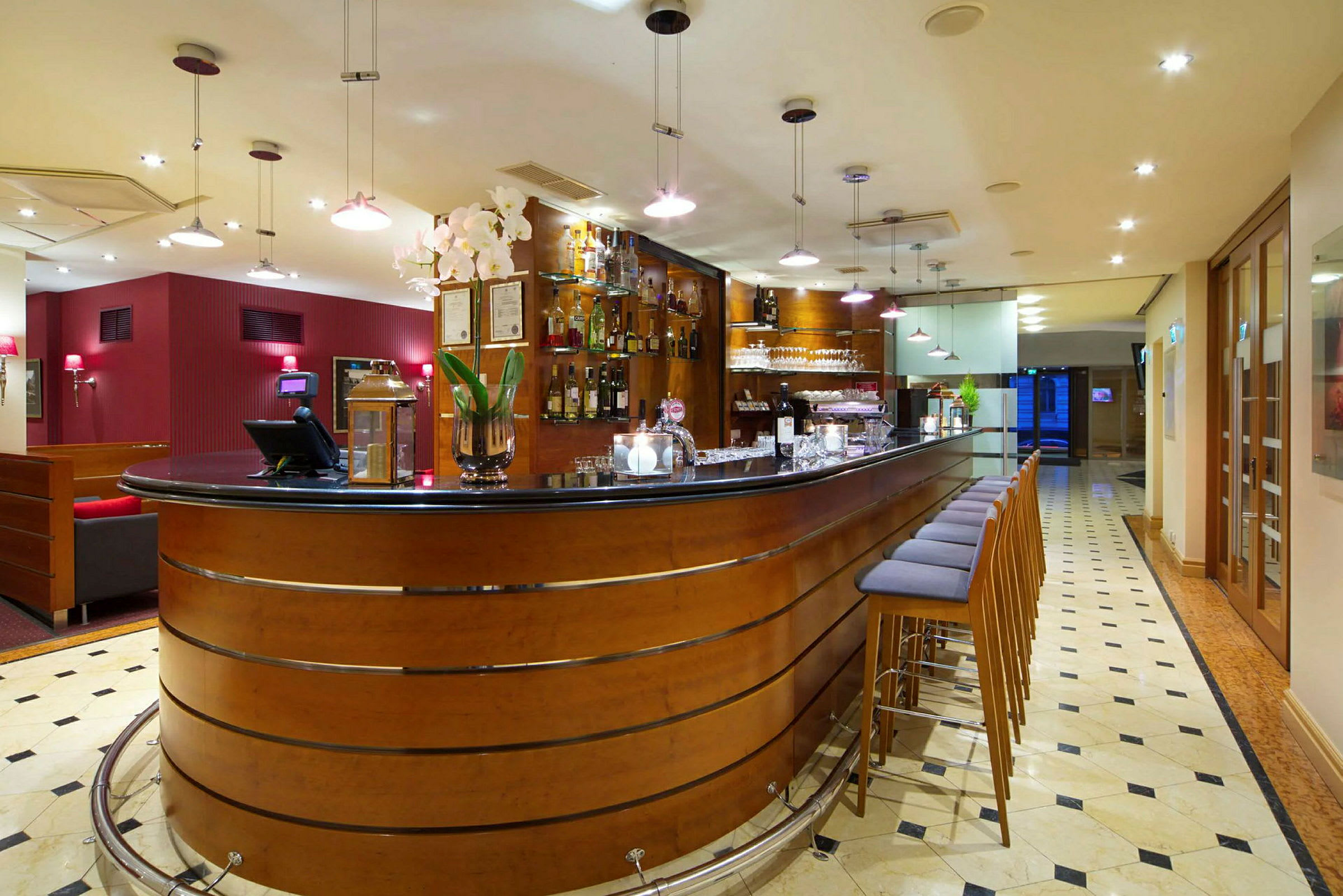 En hotellbar med en elegant design, høye stoler ved bardisken og flasker på utstilling bak. (AI-generert tekst)