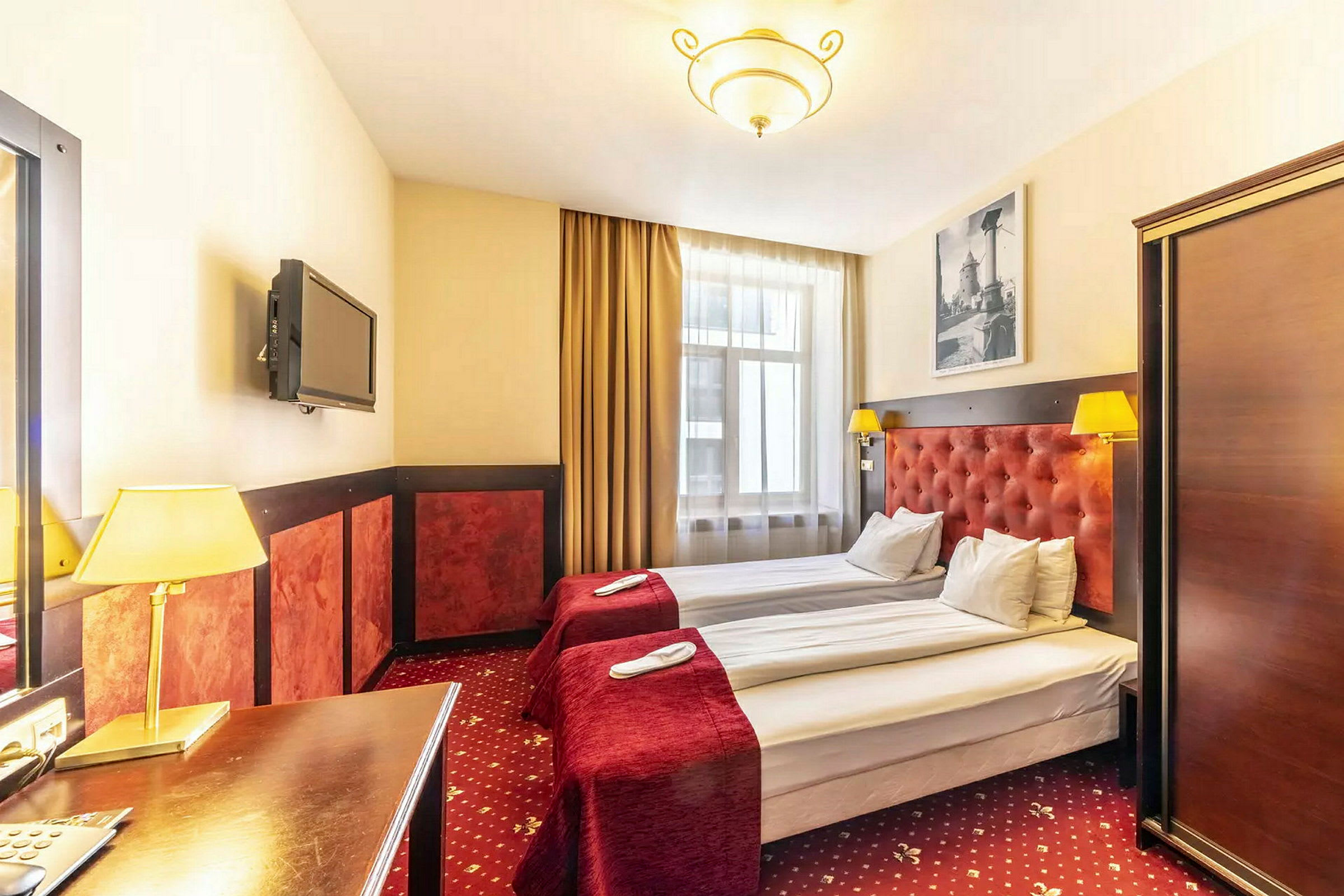 Hotellrom med to enkeltsenger, røde sengetepper og lamper. (AI-generert tekst)