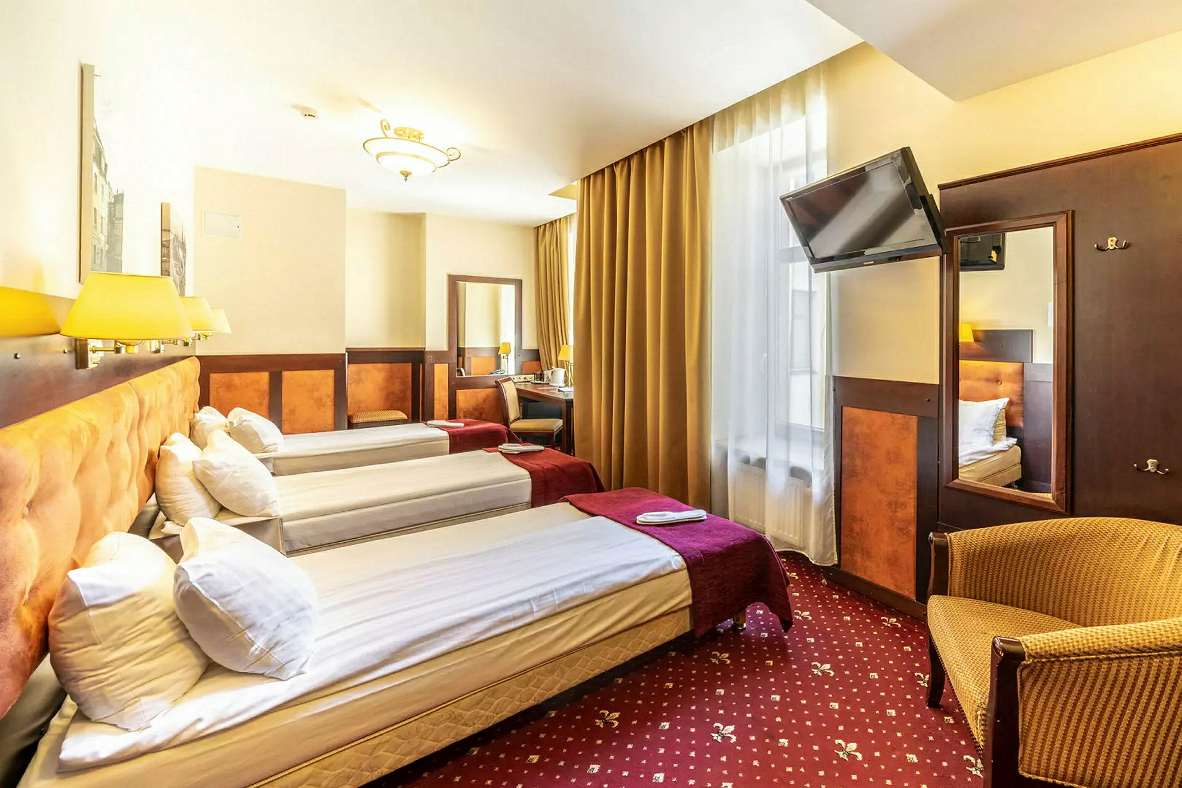 Hotellrom med tre enkeltsenger, TV, skrivebord og lenestol. (AI-generert tekst)