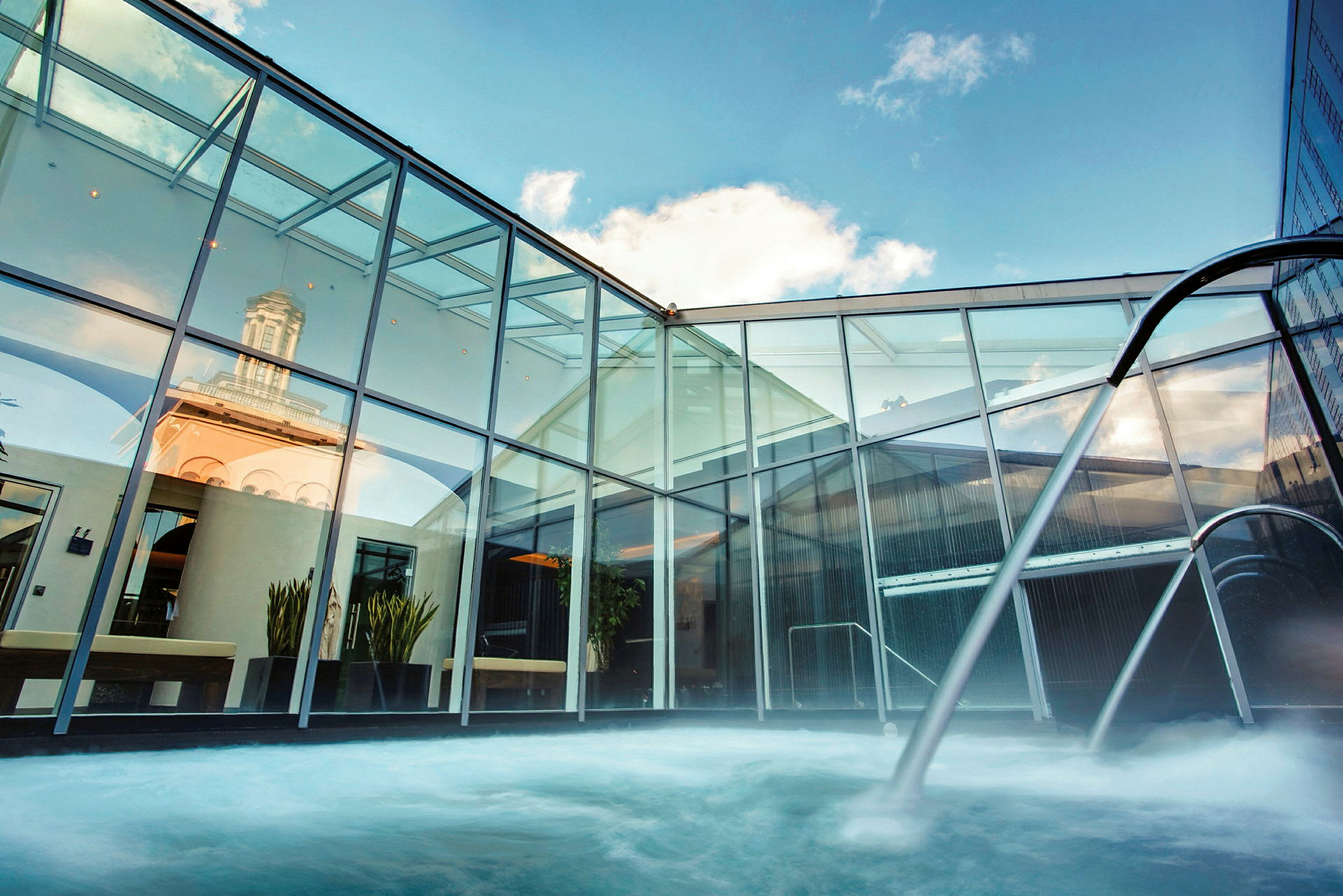 Et moderne spa med et utendørs basseng omgitt av glassvegger og himmel i bakgrunnen. (AI-generert tekst)