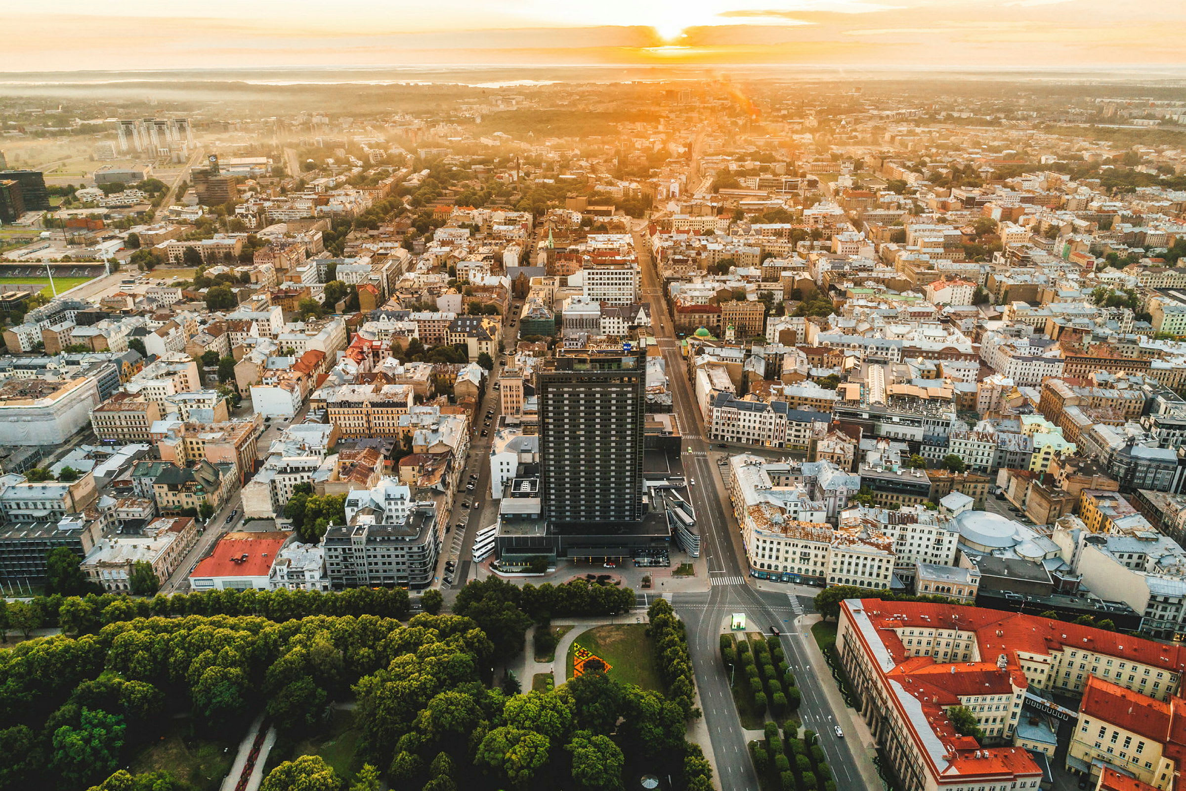 Flyfoto over en by med bygninger, veier og parker i solnedgangen. (AI-generert tekst)