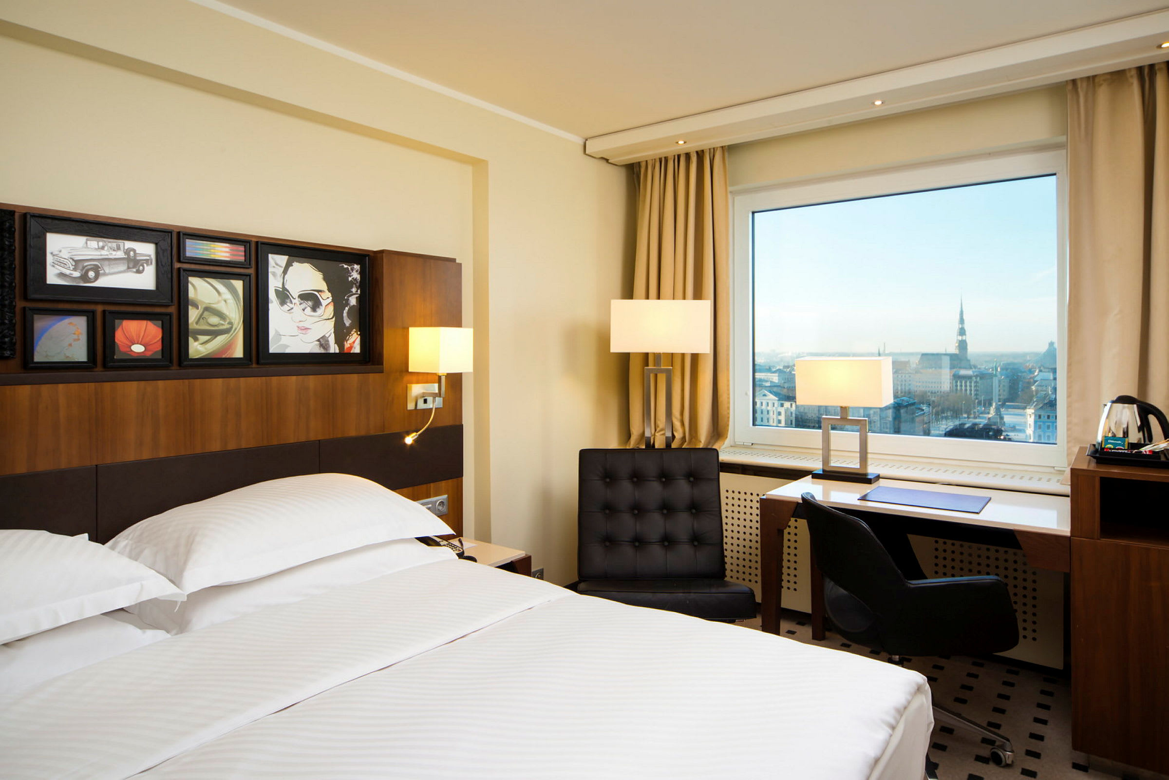 Hotellrom med en stor seng, moderne møbler og et stort vindu med utsikt over en by. (AI-generert tekst)