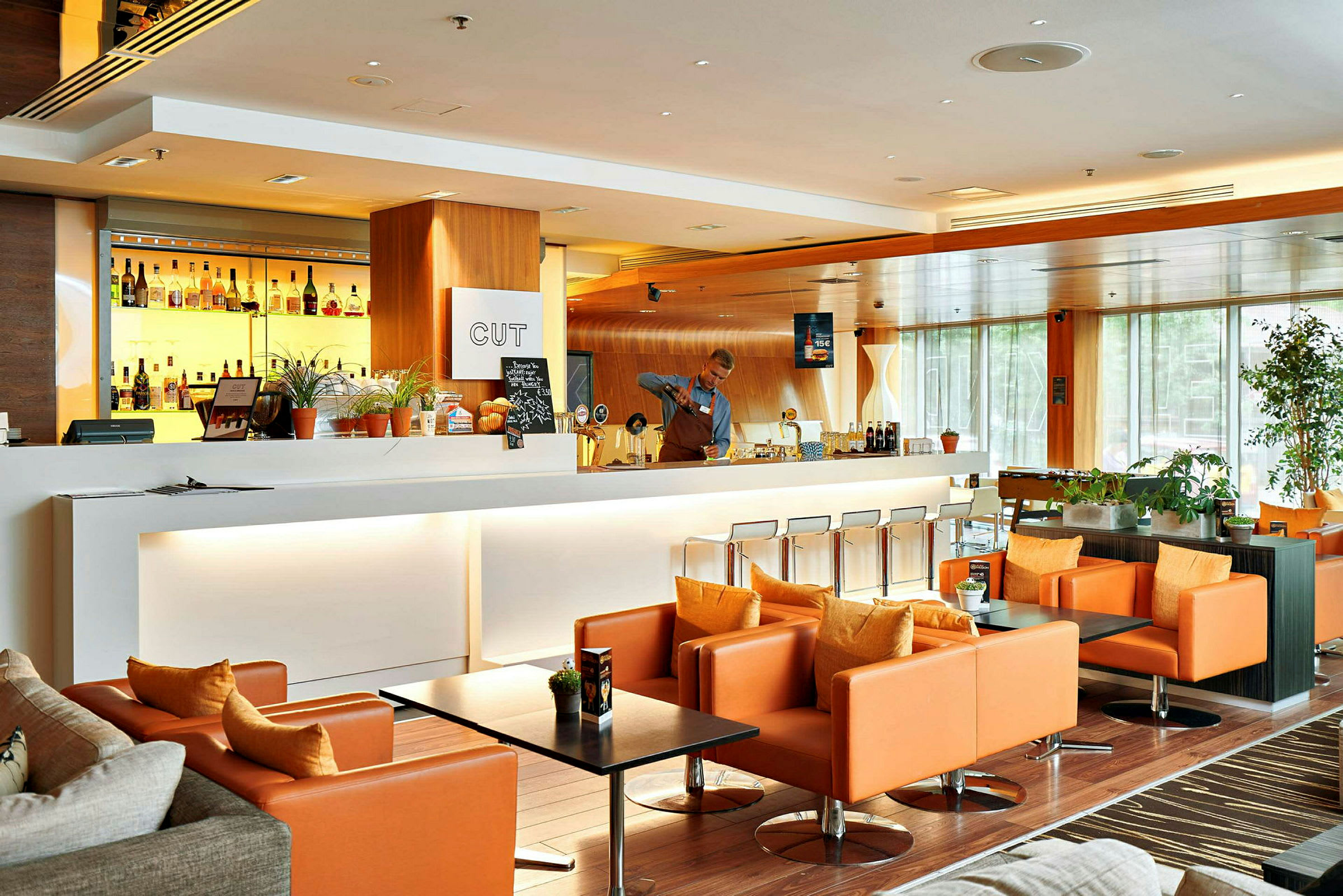 En moderne og elegant lounge med en hvit bardisk, bakgrunnsbelyste brennevinsflasker og komfortable oransje lenestoler. (AI-generert tekst)