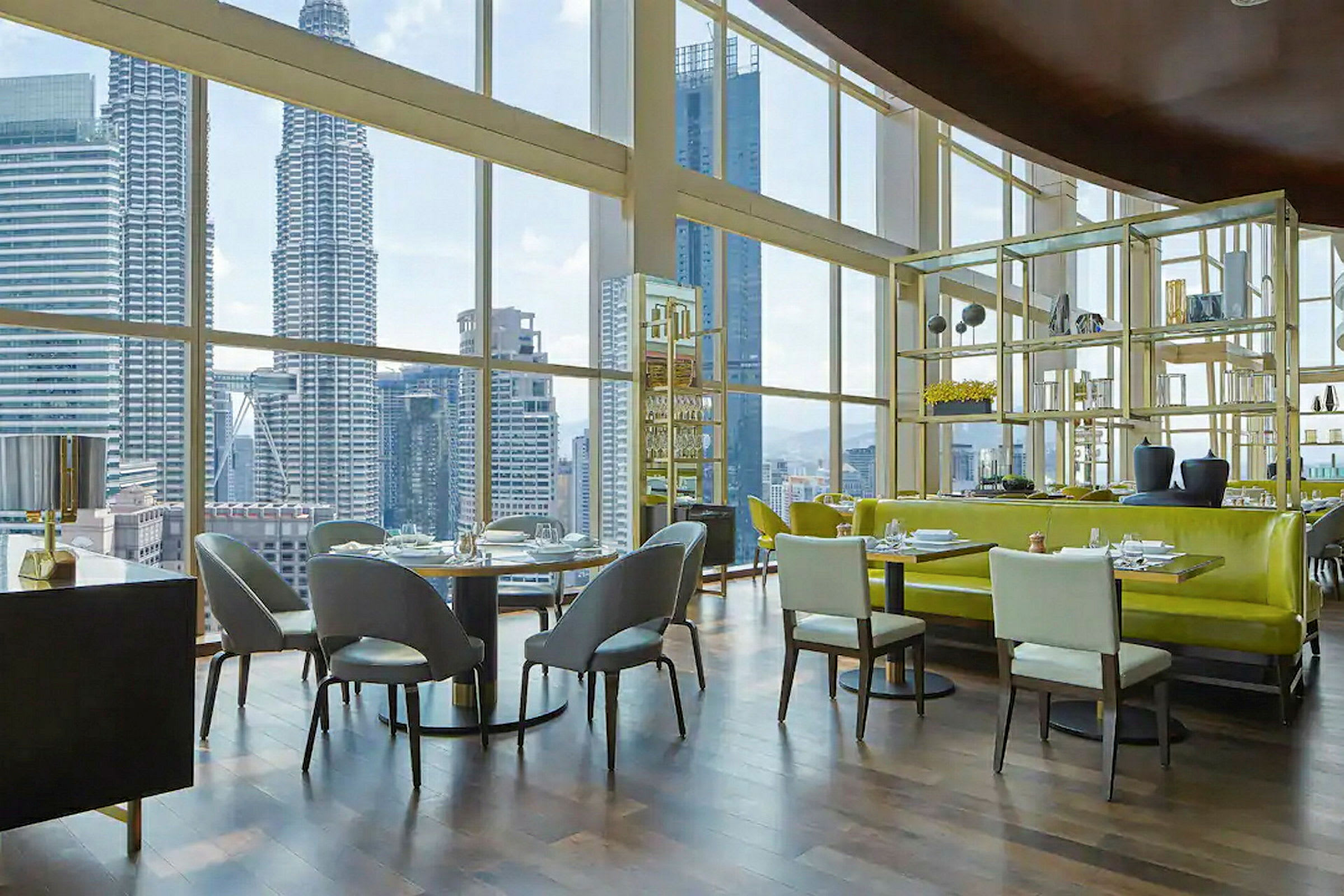Interiør av en moderne restaurant med store vinduer som gir utsikt over en byens skyline inkludert høyhus. (AI-generert tekst)