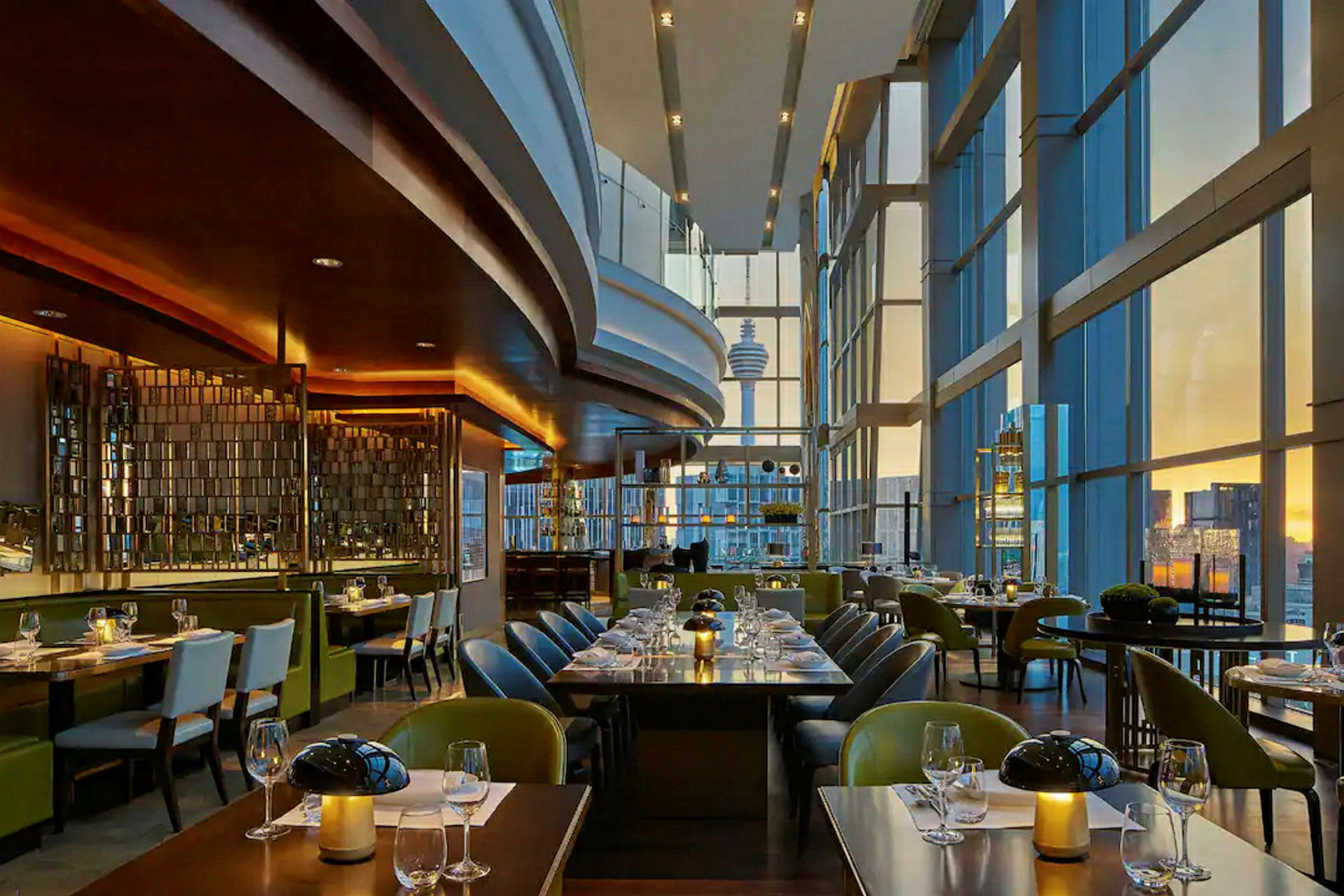 Restaurant med moderne møbler og store panoramavinduer med utsikt over en by ved solnedgang. (AI-generert tekst)