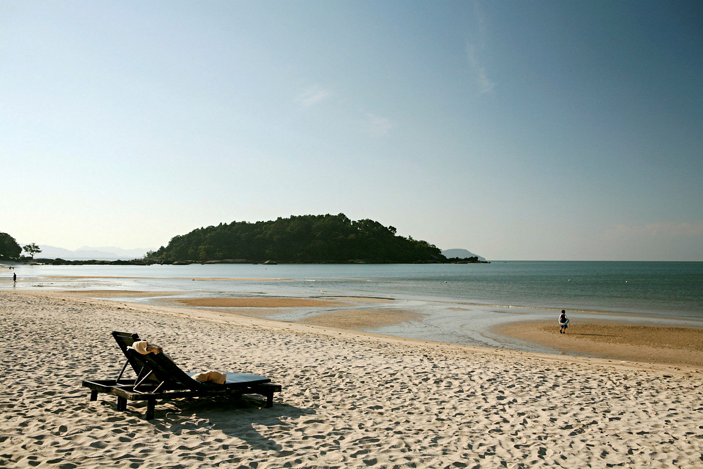 Bilde av en rolig strand med en solseng i forgrunnen og en liten øy i det fjerne. (AI-generert tekst)