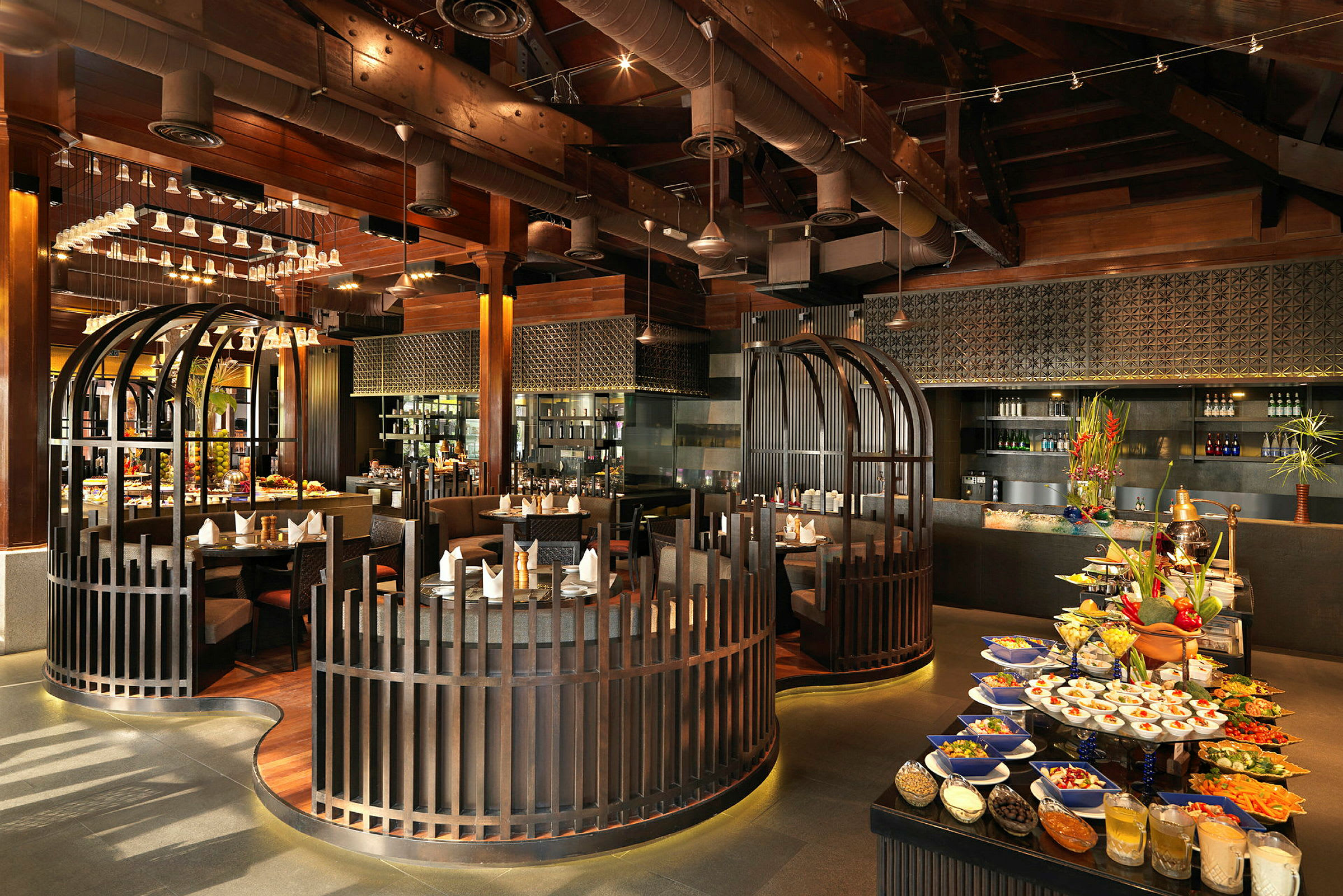 En restaurant med elegant interiør som inkluderer sitteplasser omgitt av trerekkverk, en matbuffé med fargerike retter og drikkevarer, samt en moderne atmosfære med synlige takstrukturer. (AI-generert tekst)