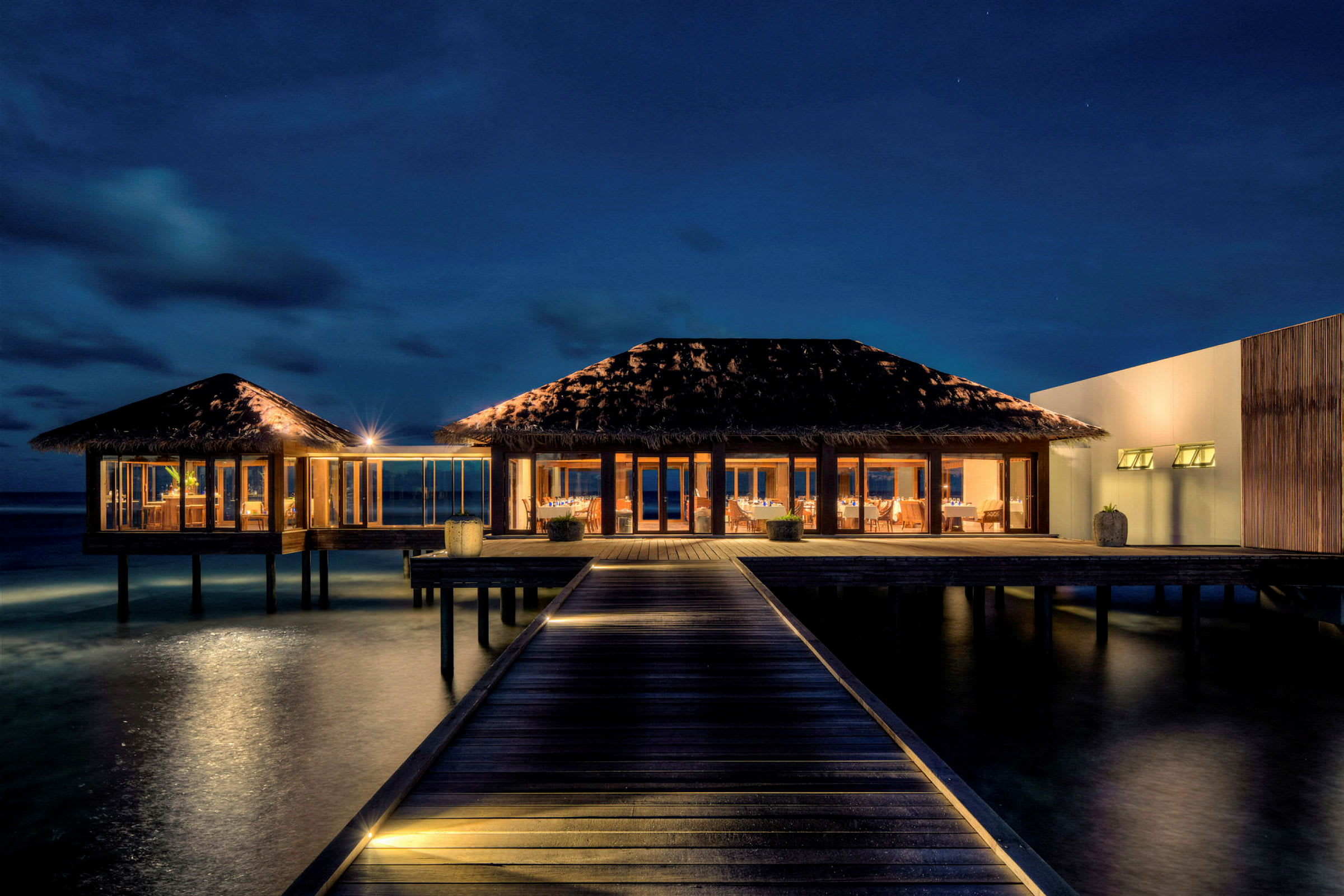 Bilde av en opplyst strandvilla på påler over havet, fotografert om natten. (AI-generert tekst)