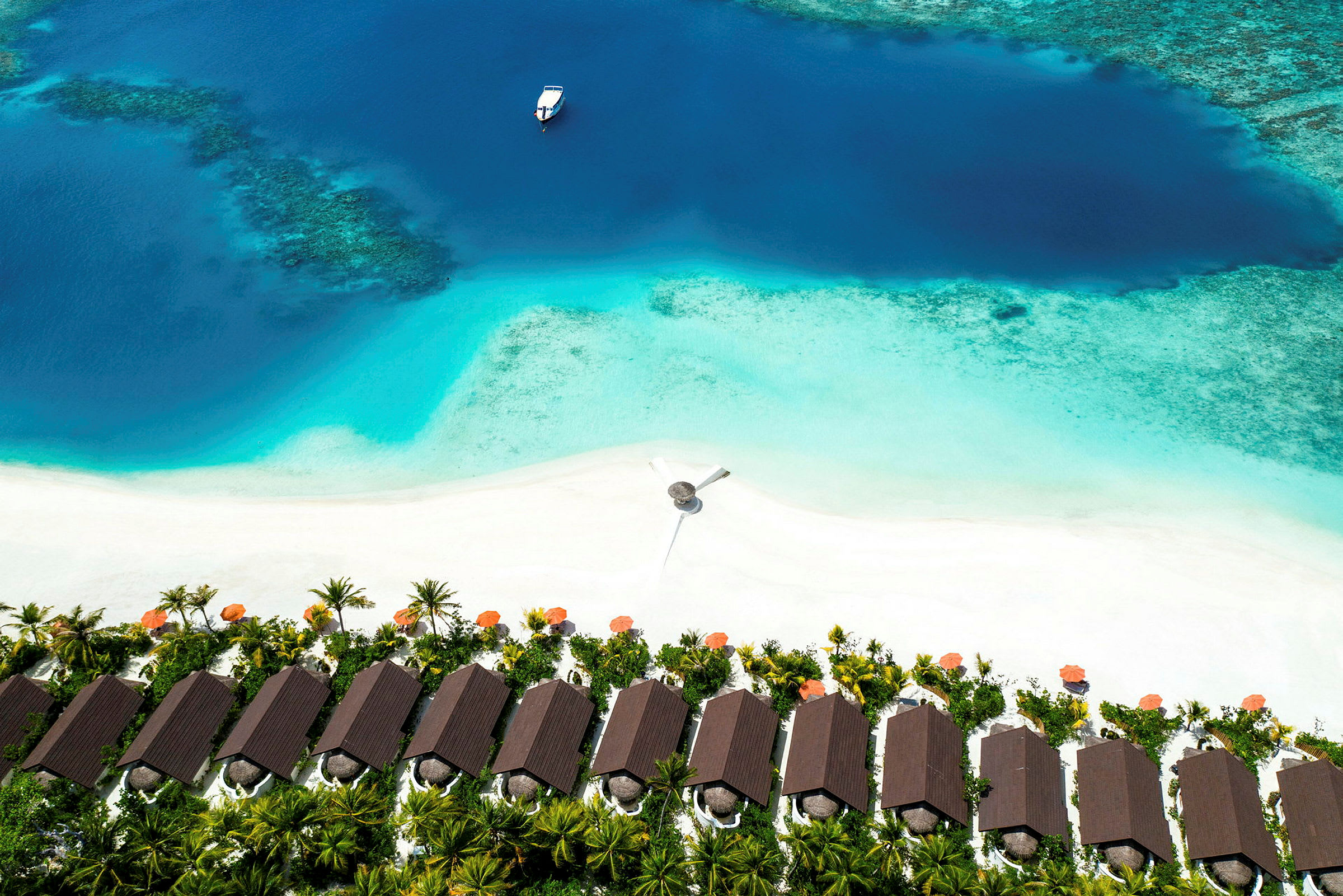 Flyfoto av tropiske strandhytter ved en hvit sandstrand med turkist vann og en båt på havet. (AI-generert tekst)