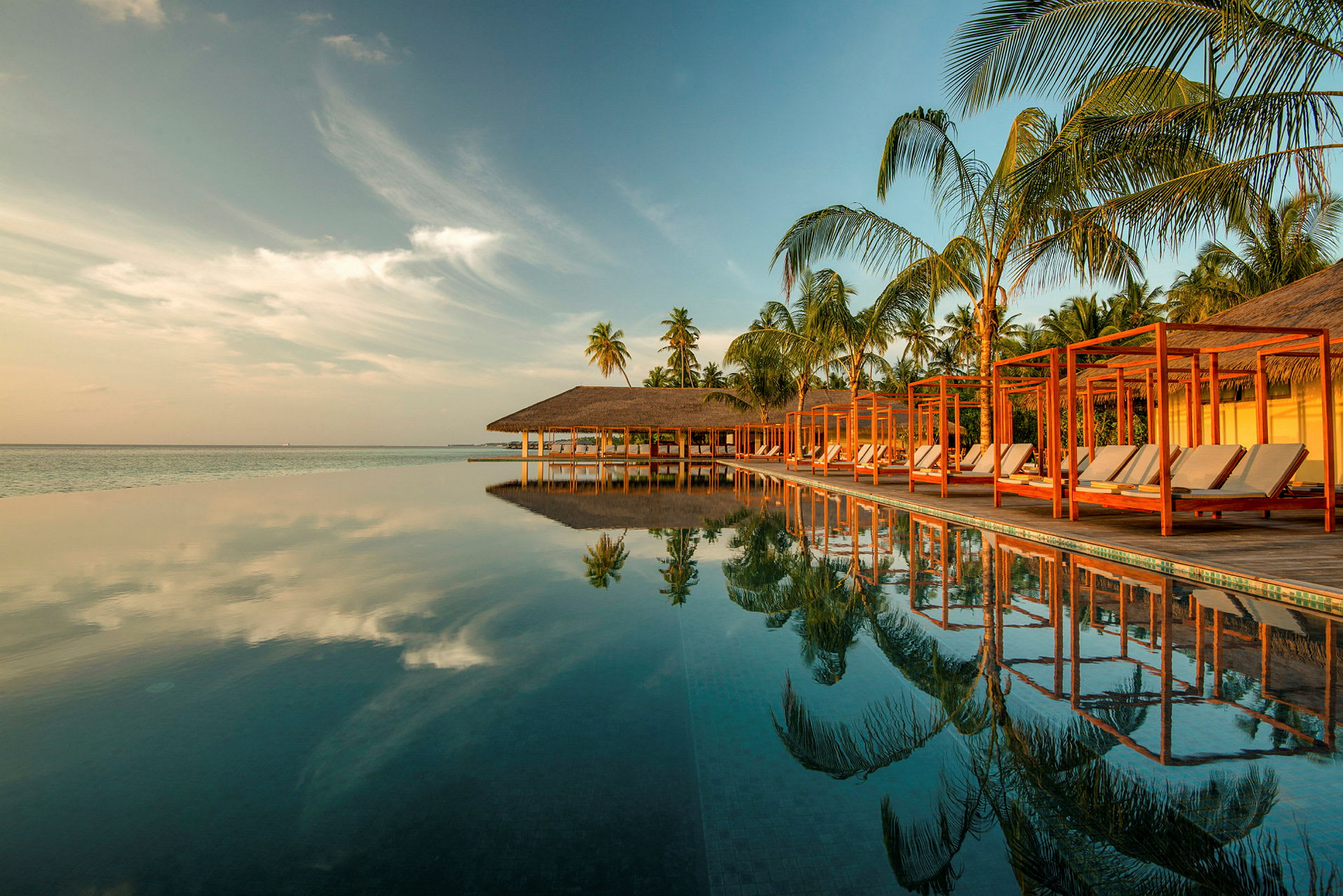 En infinitypool ved en tropisk resort med palmer og himmel som reflekteres i vannet. (AI-generert tekst)