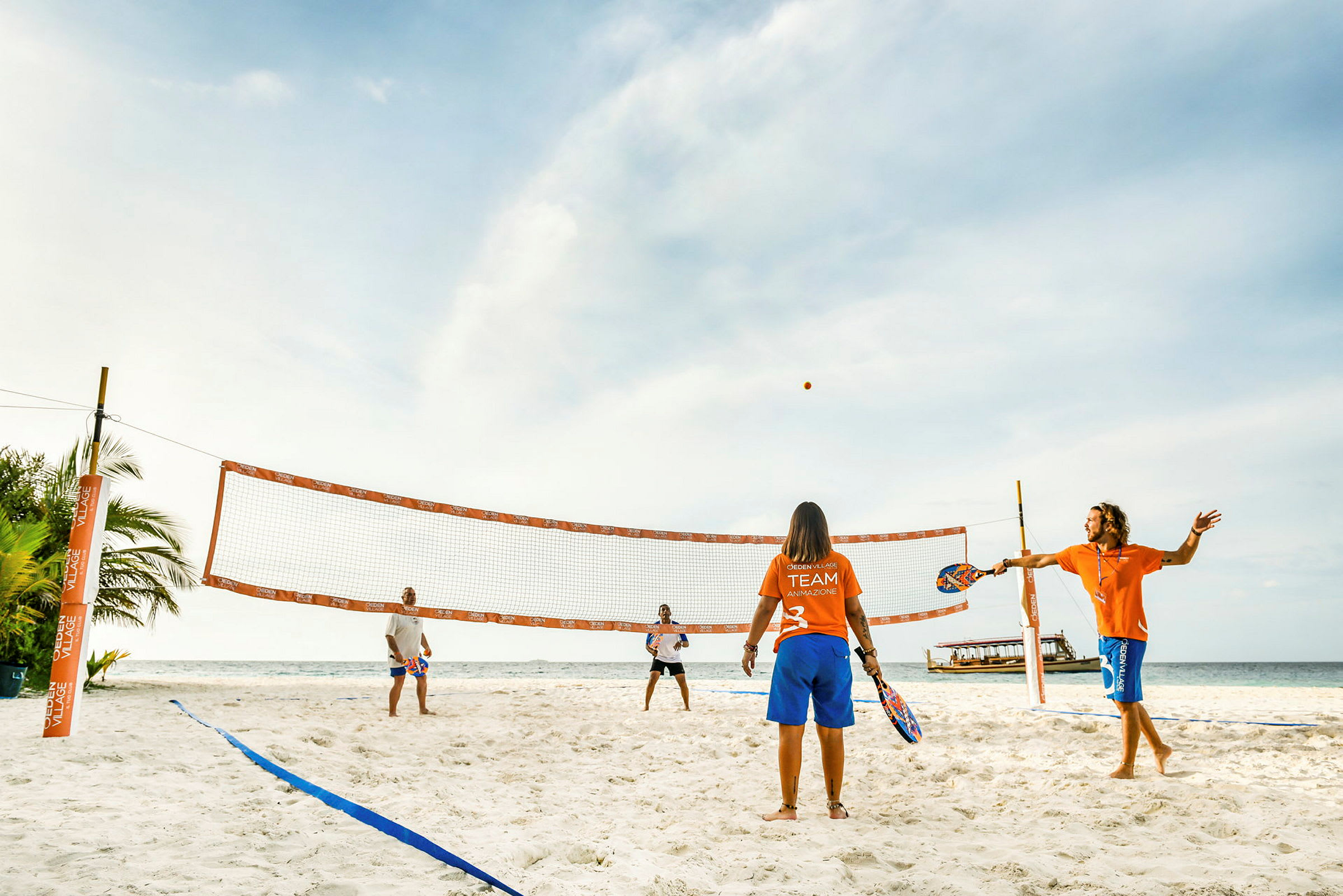 Fire personer spiller strandtennis på en solfylt sandstrand. (AI-generert tekst)