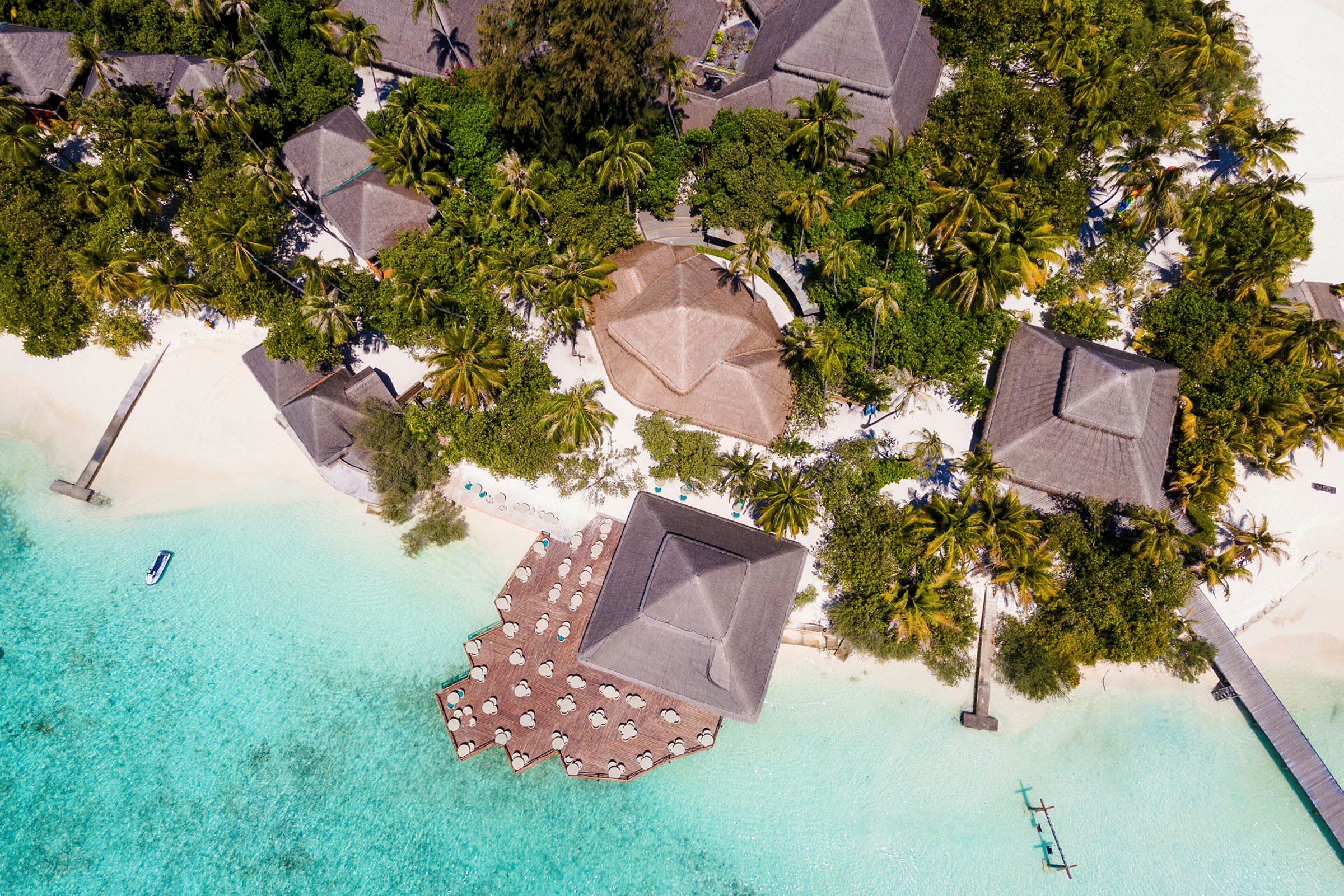 Flyfoto av tropisk resort med bungalower omgitt av frodig vegetasjon og klart blått vann. (AI-generert tekst)
