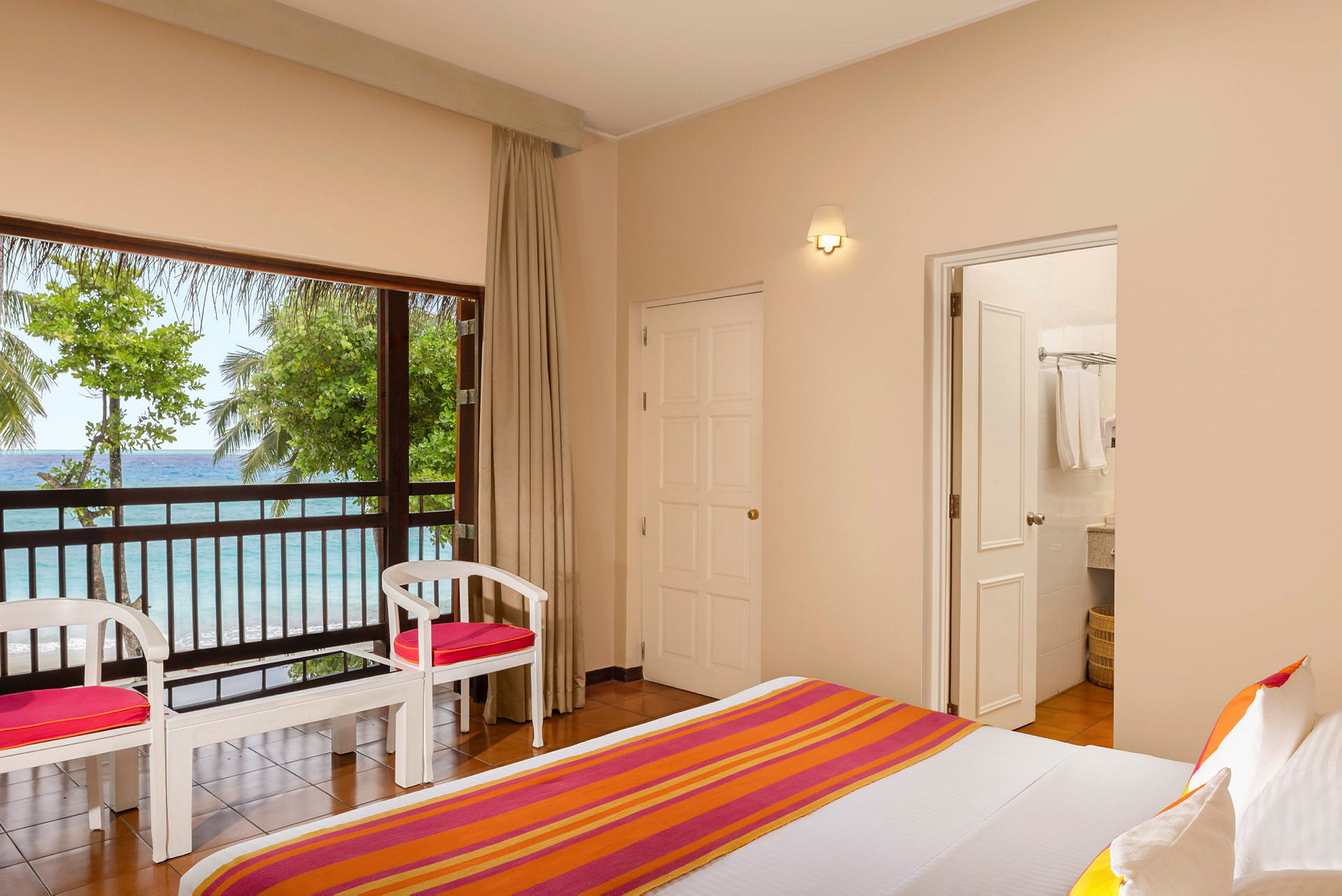 Et hotellrom med seng og tremøbler, utsikt mot havet og grøntområder utenfor vinduet. (AI-generert tekst)